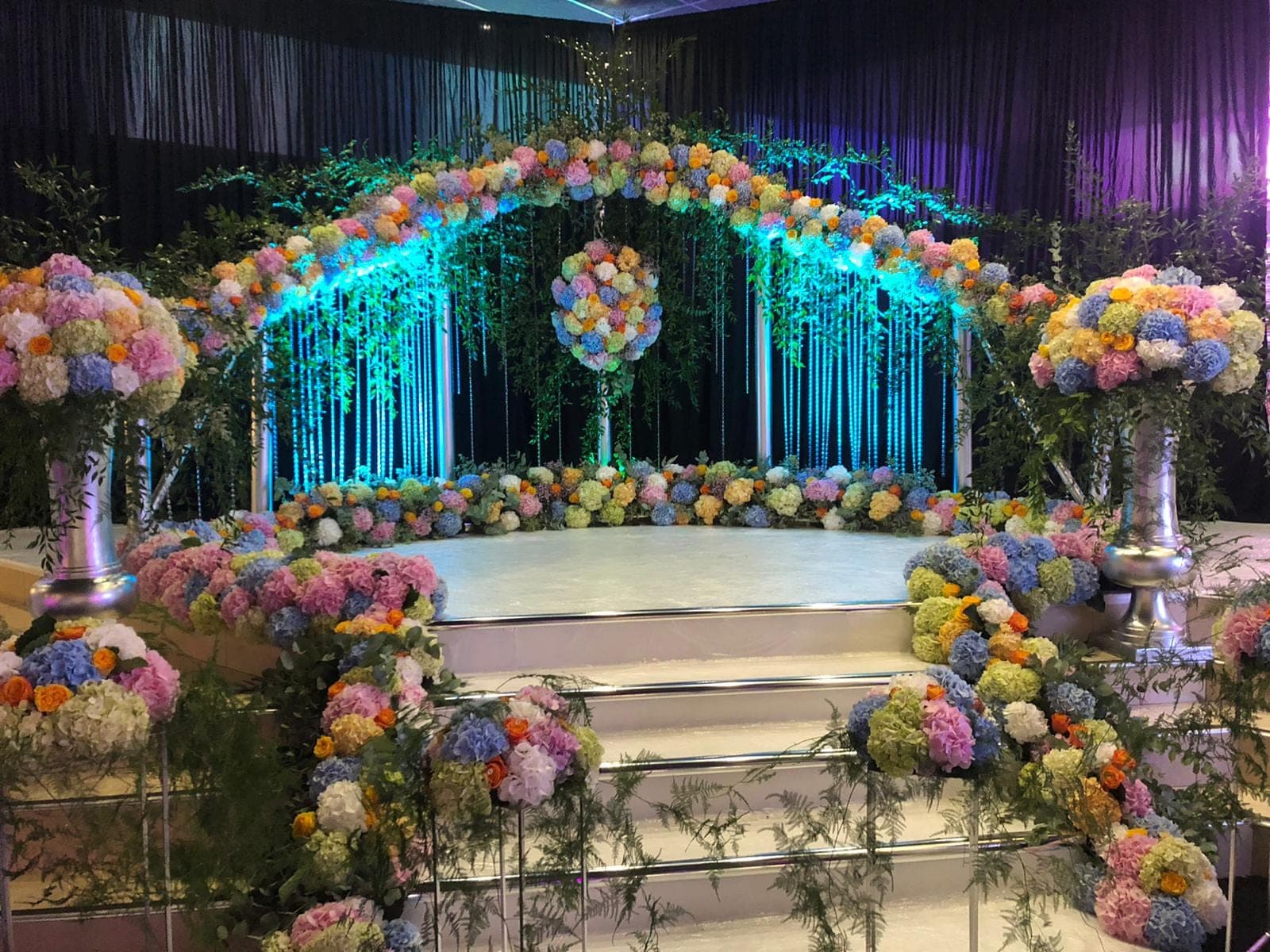 A stage decorated with colorful flowers and blue lights for a wedding ceremony.