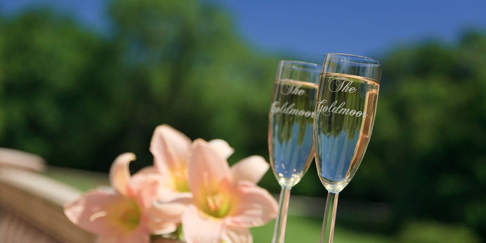Two champagne flutes with etched venue name and pink flowers.