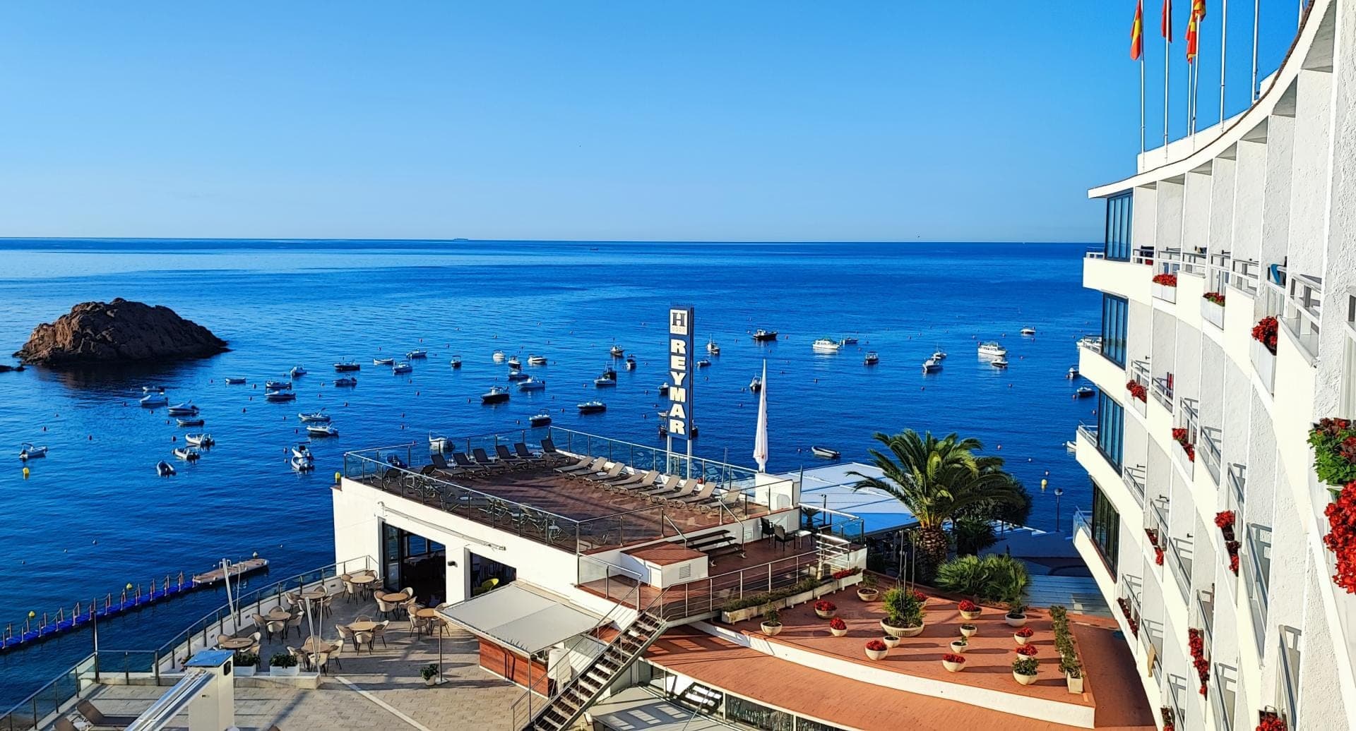 Hotel building with balconies overlooking the sea and boats in the water.