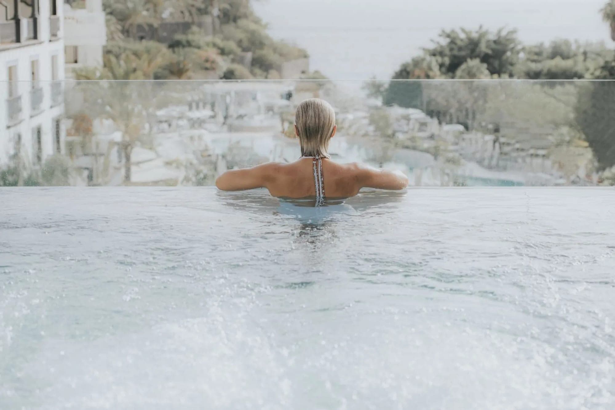 Woman in an infinity pool overlooking the ocean and buildings.