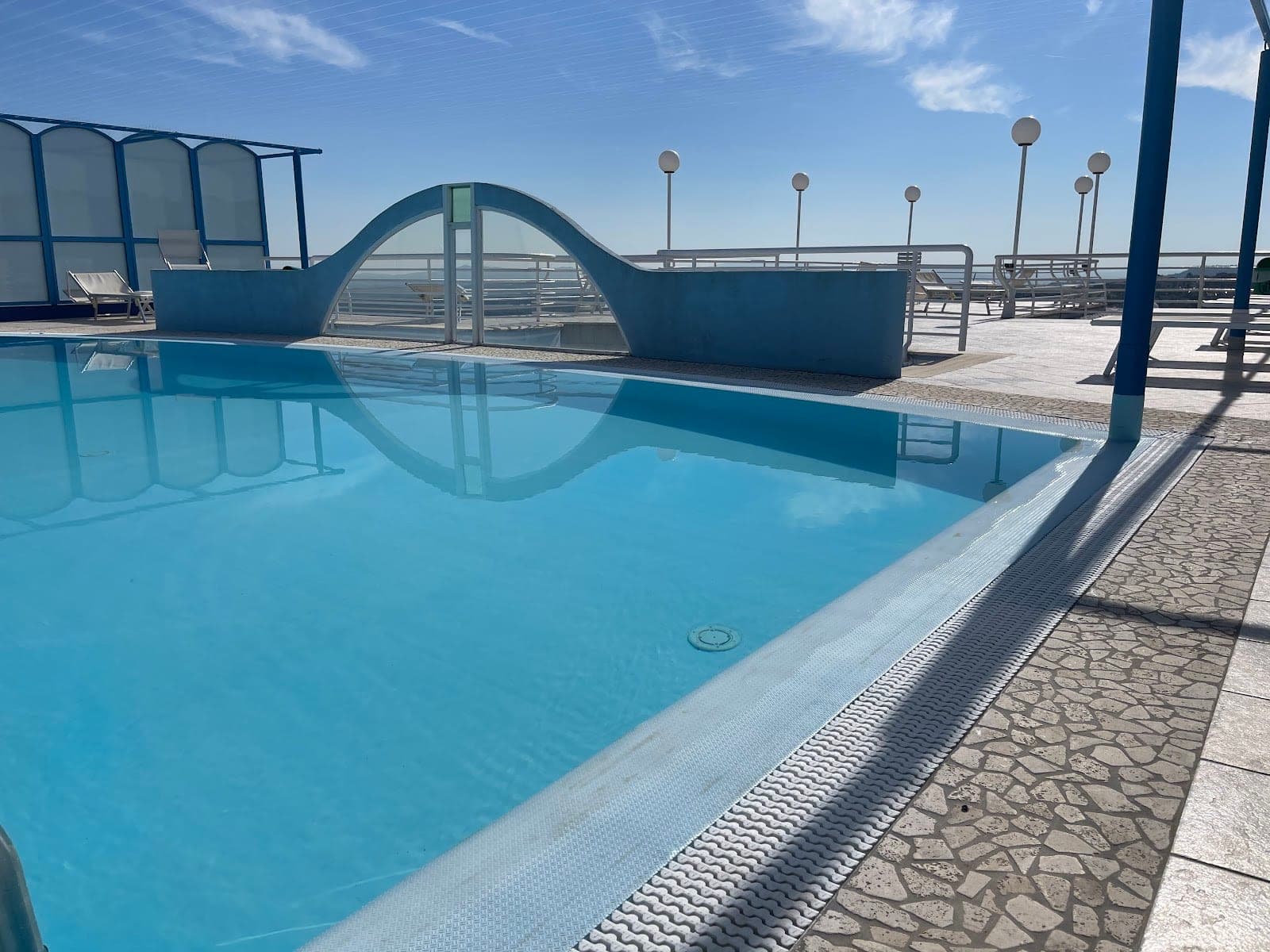 A swimming pool with blue water and lounge chairs on the deck under a clear sky.