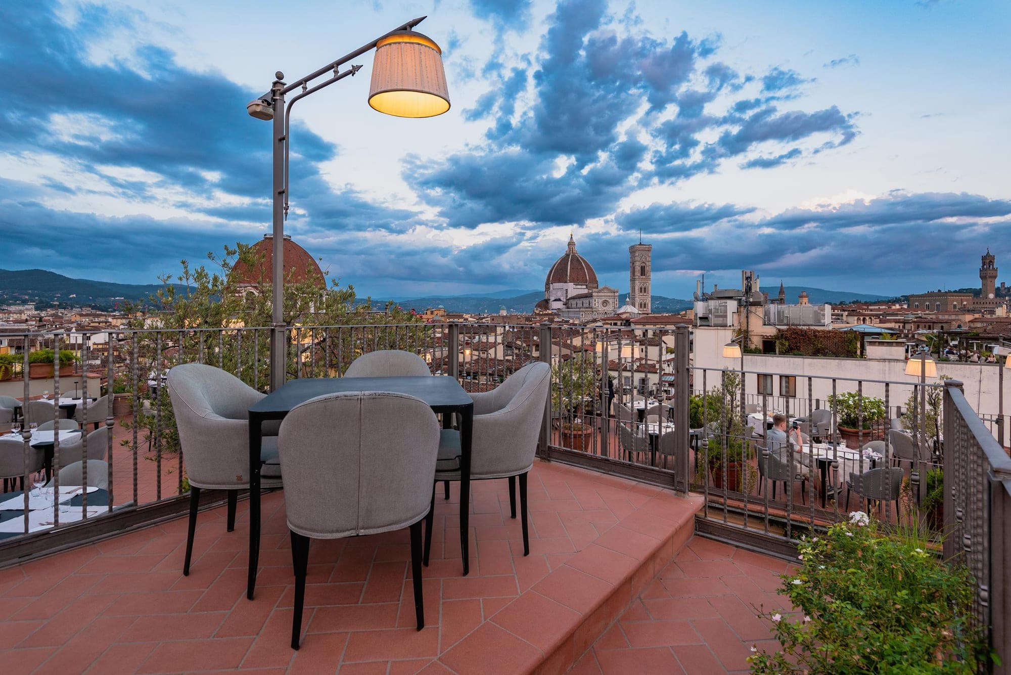 Rooftop terrace with tables and chairs overlooking Florence at dusk.