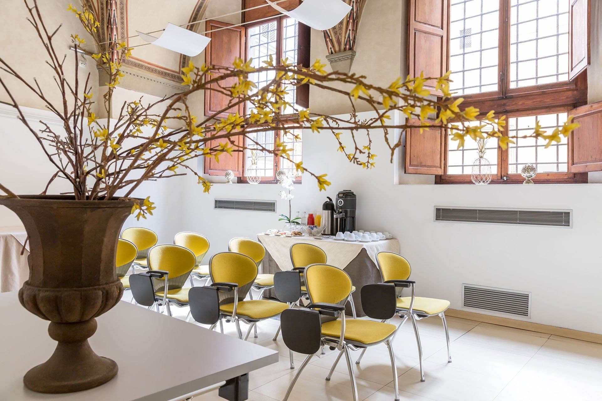Chairs and a coffee station in a room with large windows.