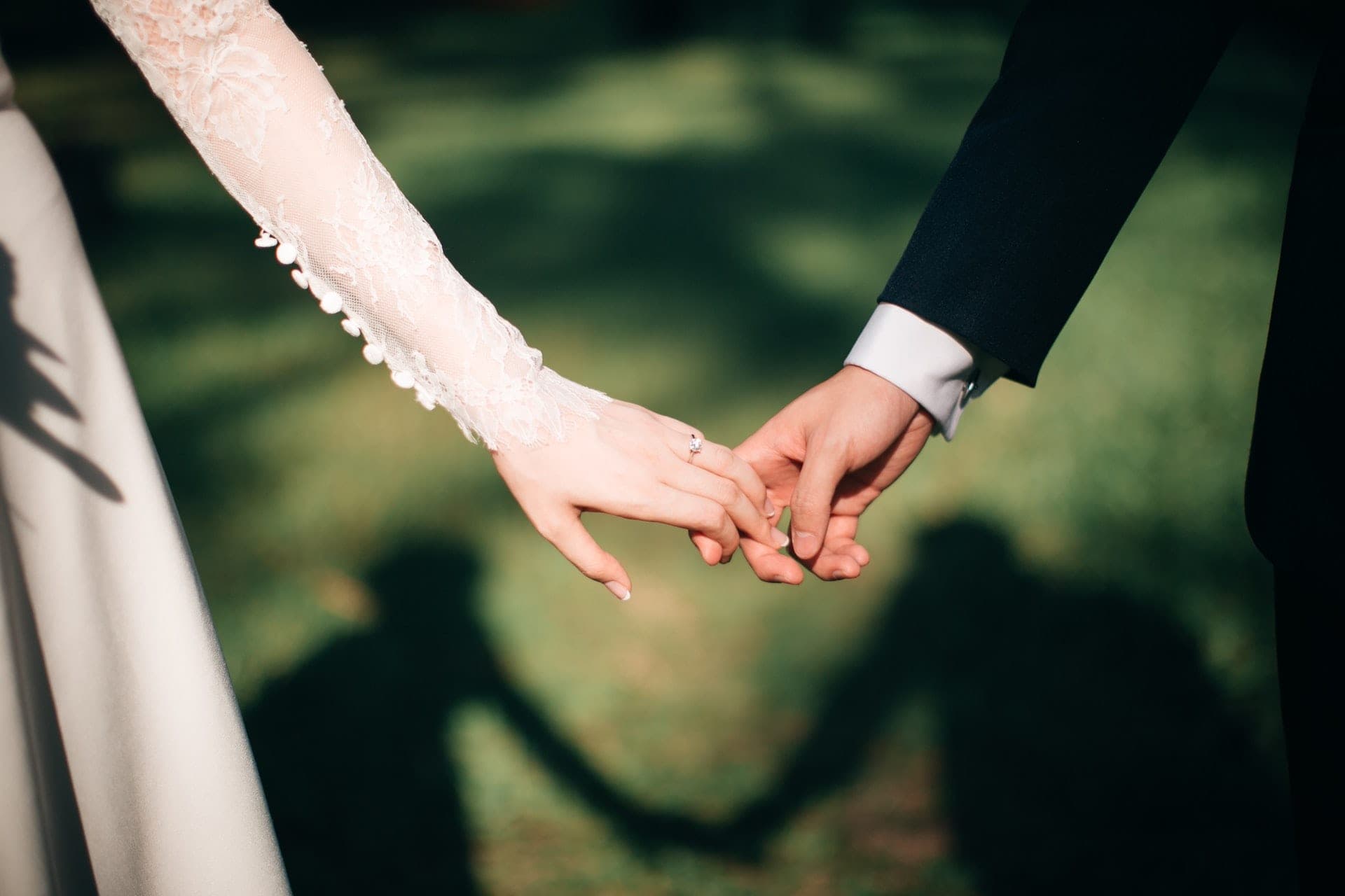 Bride and groom holding hands outdoors with shadows on the grass.