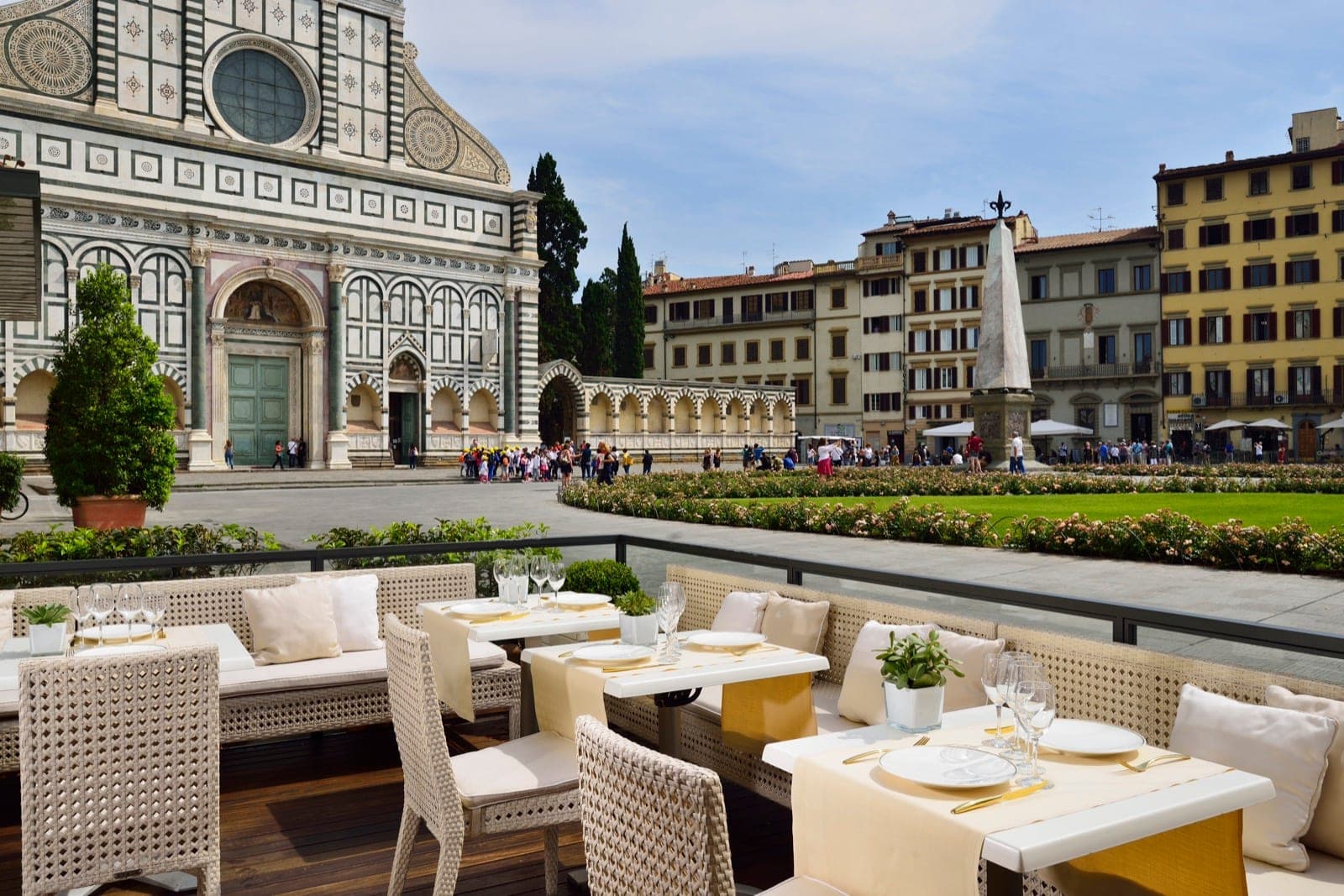 Outdoor dining terrace with tables set for a meal, overlooking a historic square and building.
