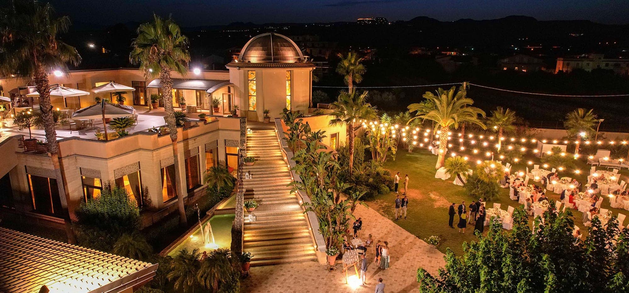 Outdoor reception area at night with tables and string lights.