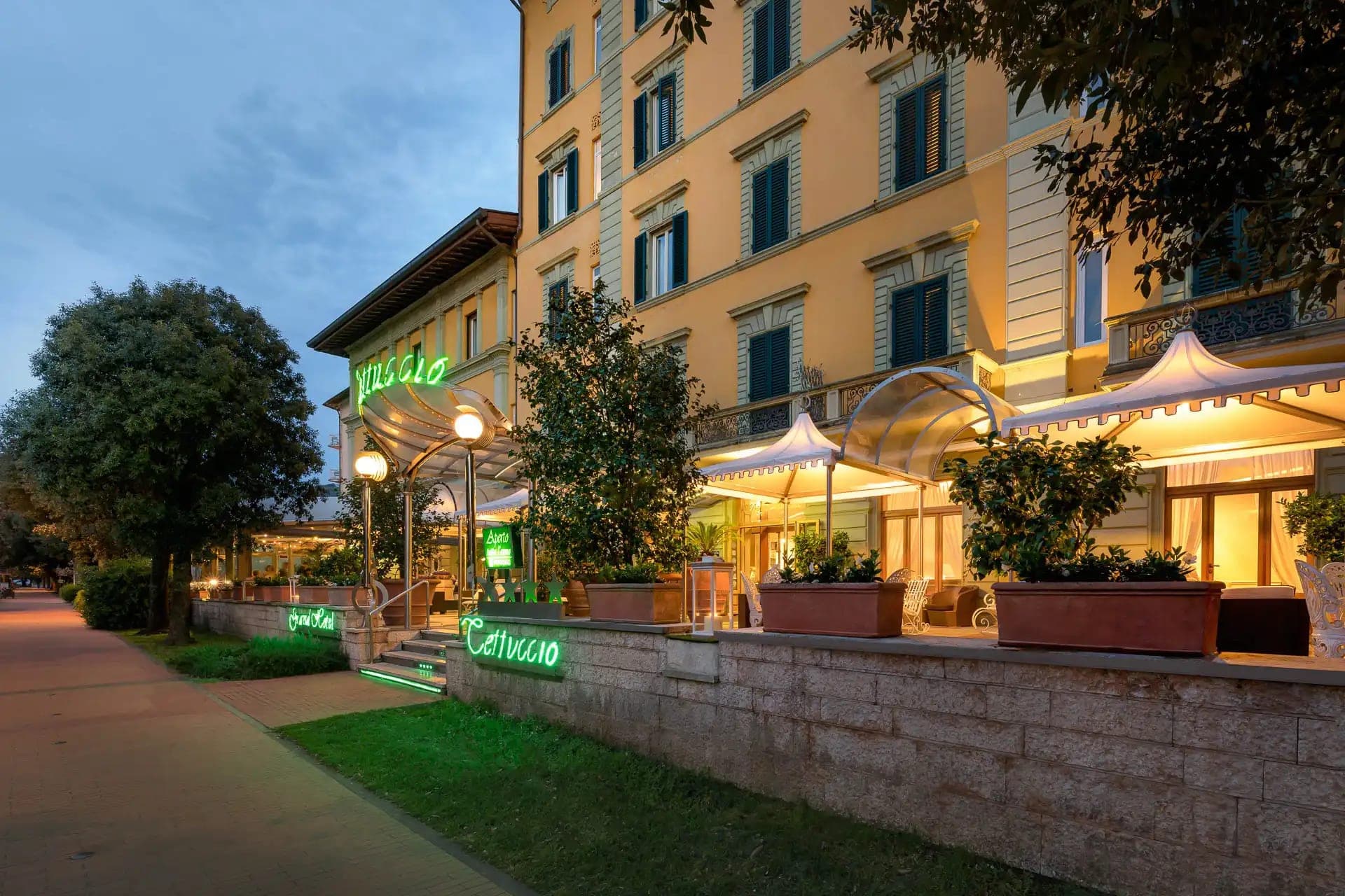Exterior of a yellow building with green neon signs and outdoor seating at dusk.