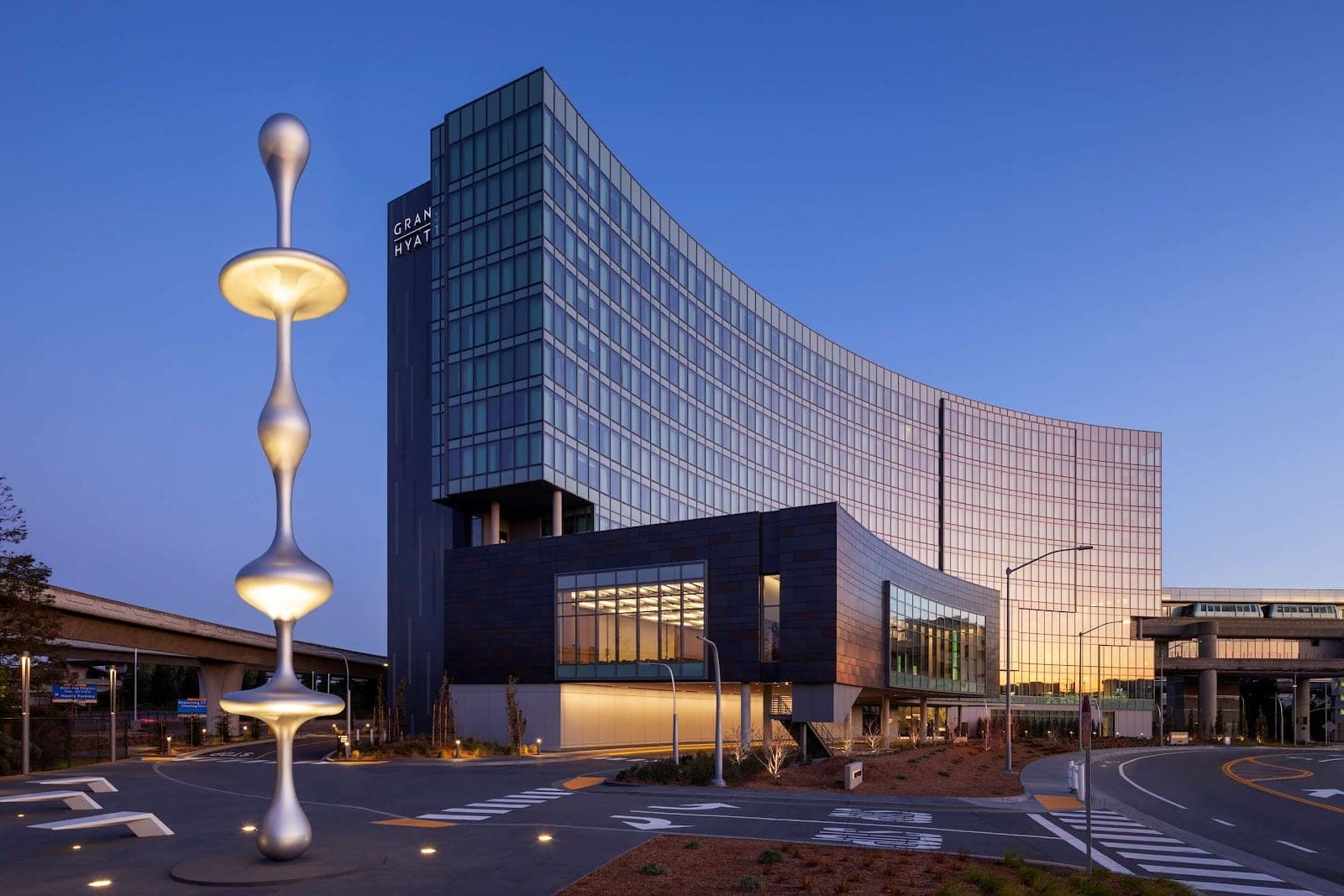 Exterior of the Grand Hyatt hotel at dusk with a modern sculpture.