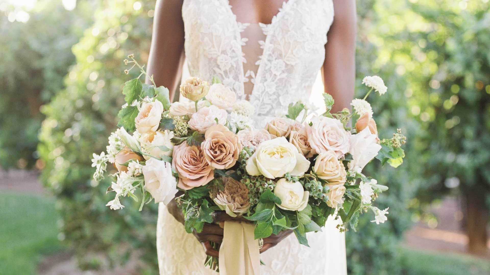 Bride holding a bouquet of roses and greenery outdoors.