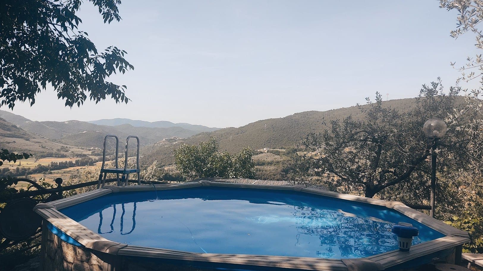 Swimming pool with a view of rolling hills and trees under a clear sky.