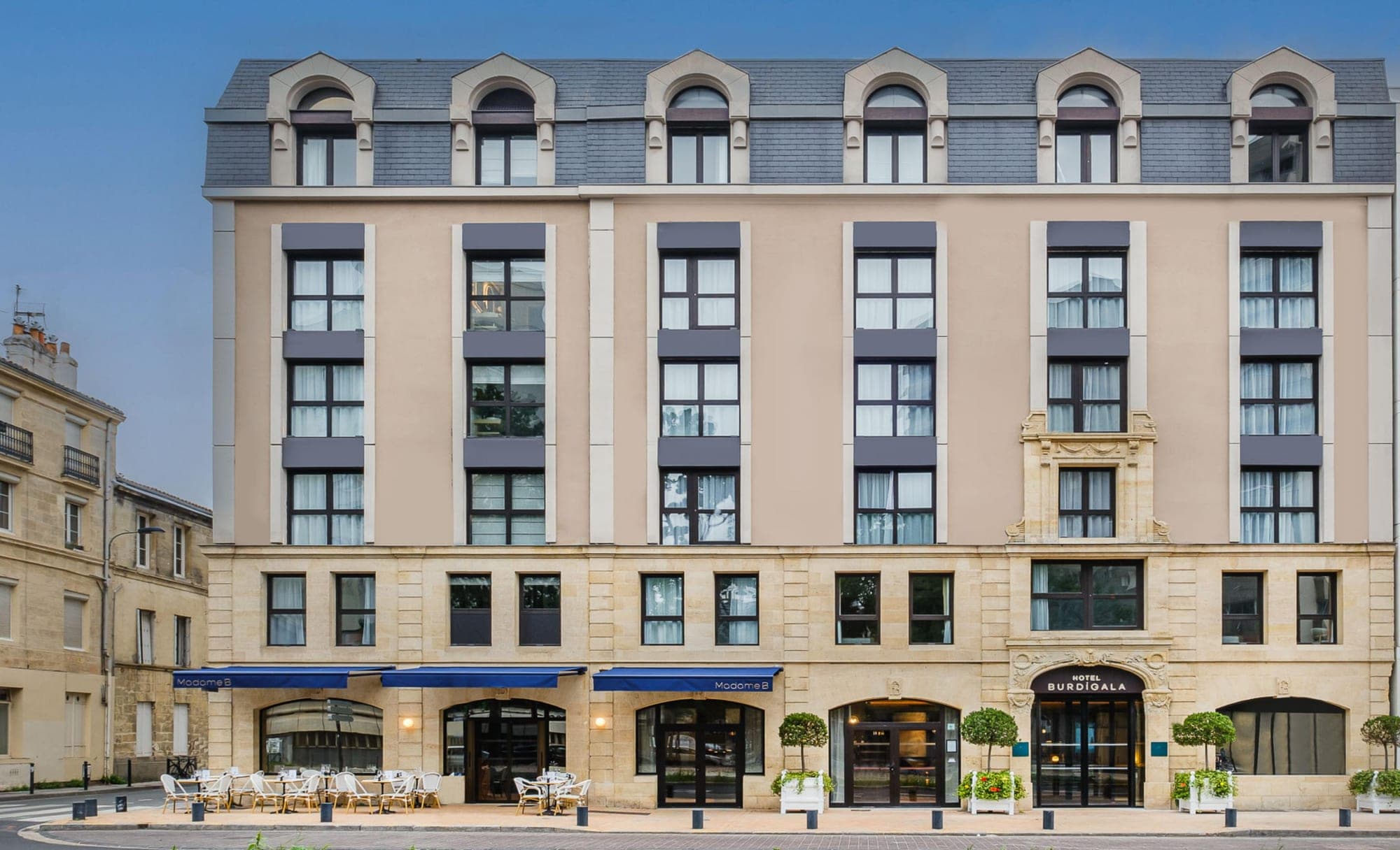 Exterior of Hotel Burdigala with blue awnings and outdoor seating.