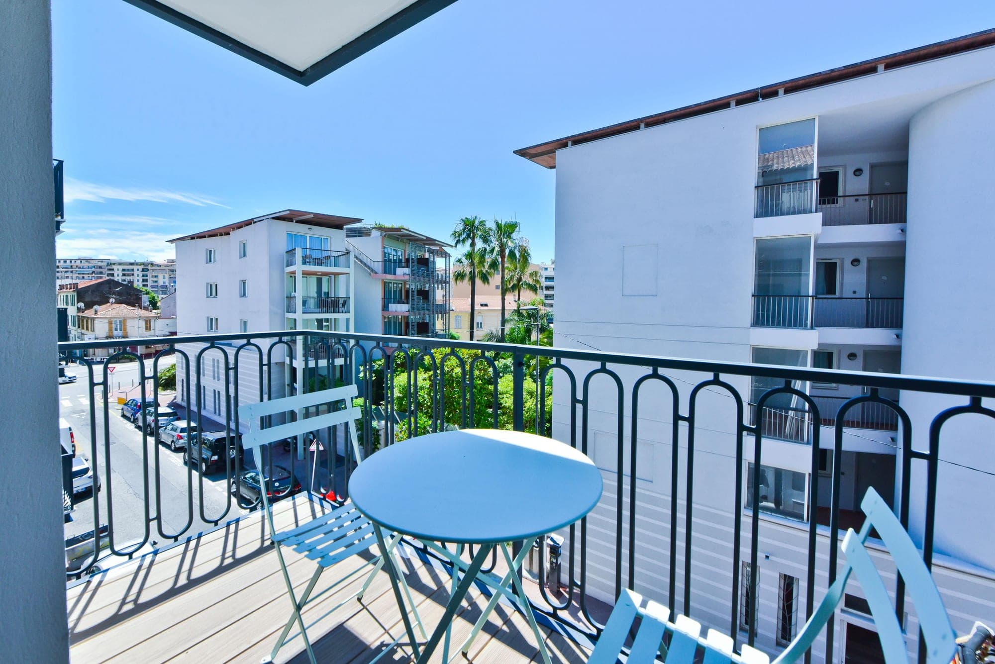 Balcony with table and chairs overlooking buildings and palm trees.