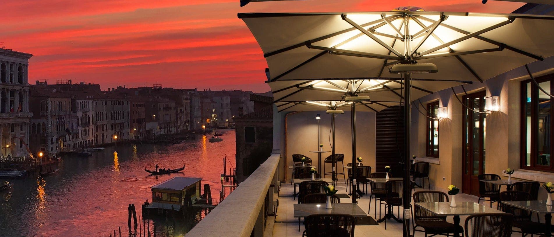 Terrace overlooking the Grand Canal in Venice at sunset with tables and chairs.