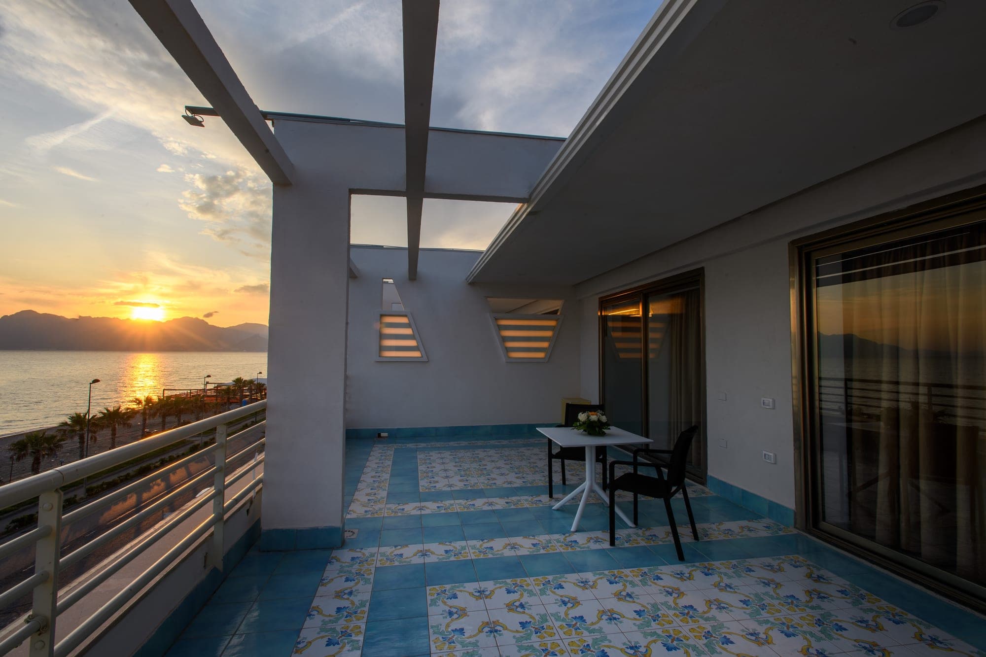 Balcony overlooking the sea at sunset with mountains in the distance.