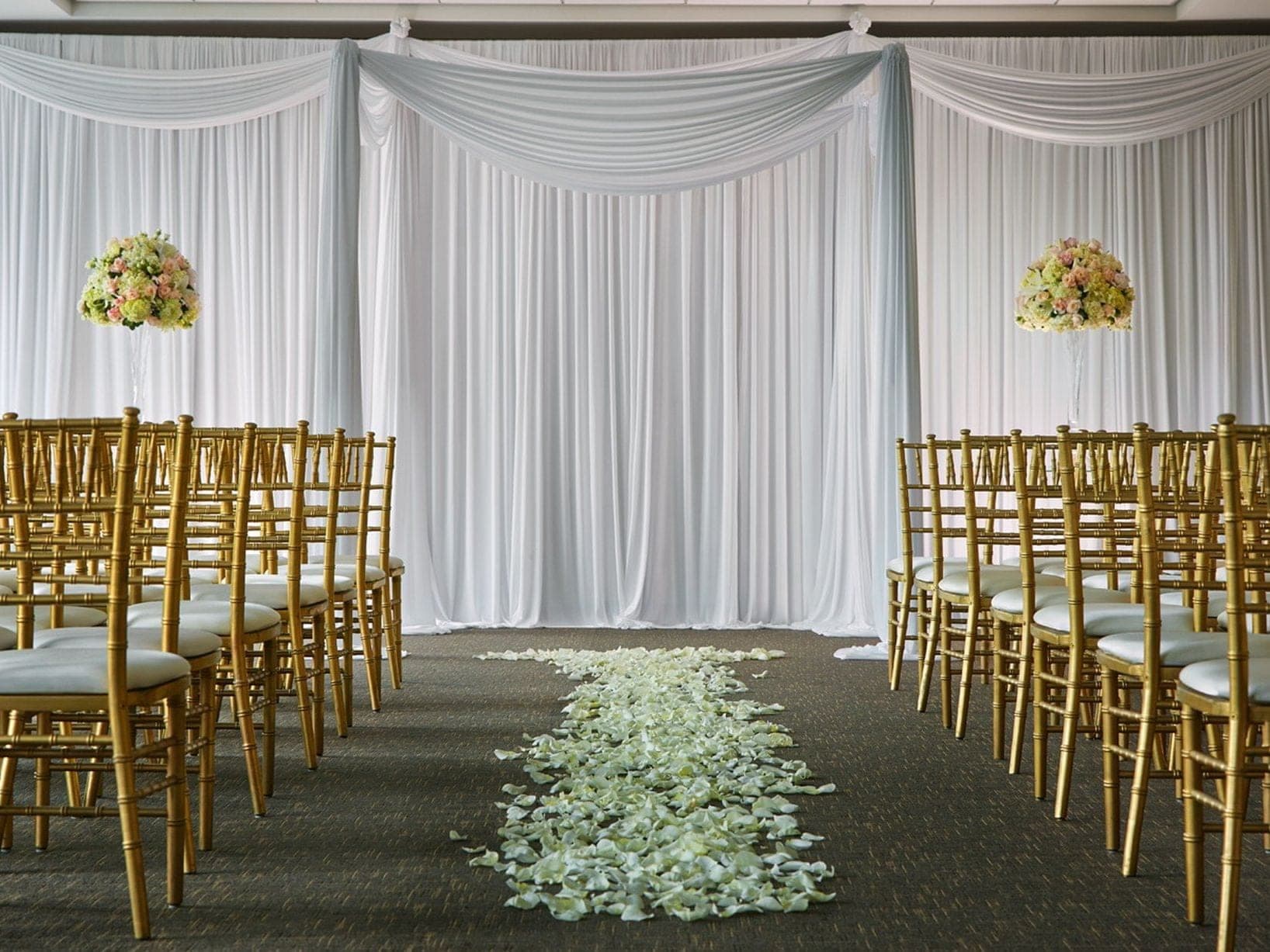 Wedding ceremony setup with gold chairs and white drapes.