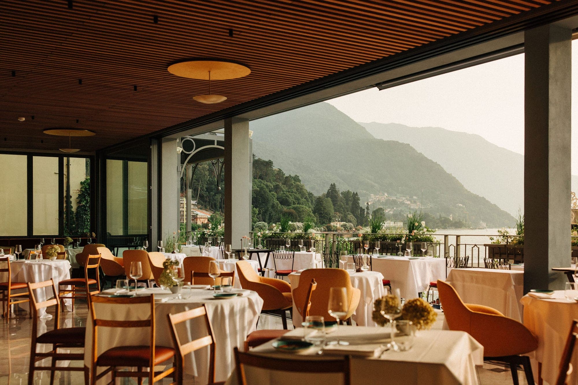 Restaurant tables set for a reception with a view of a lake and mountains.