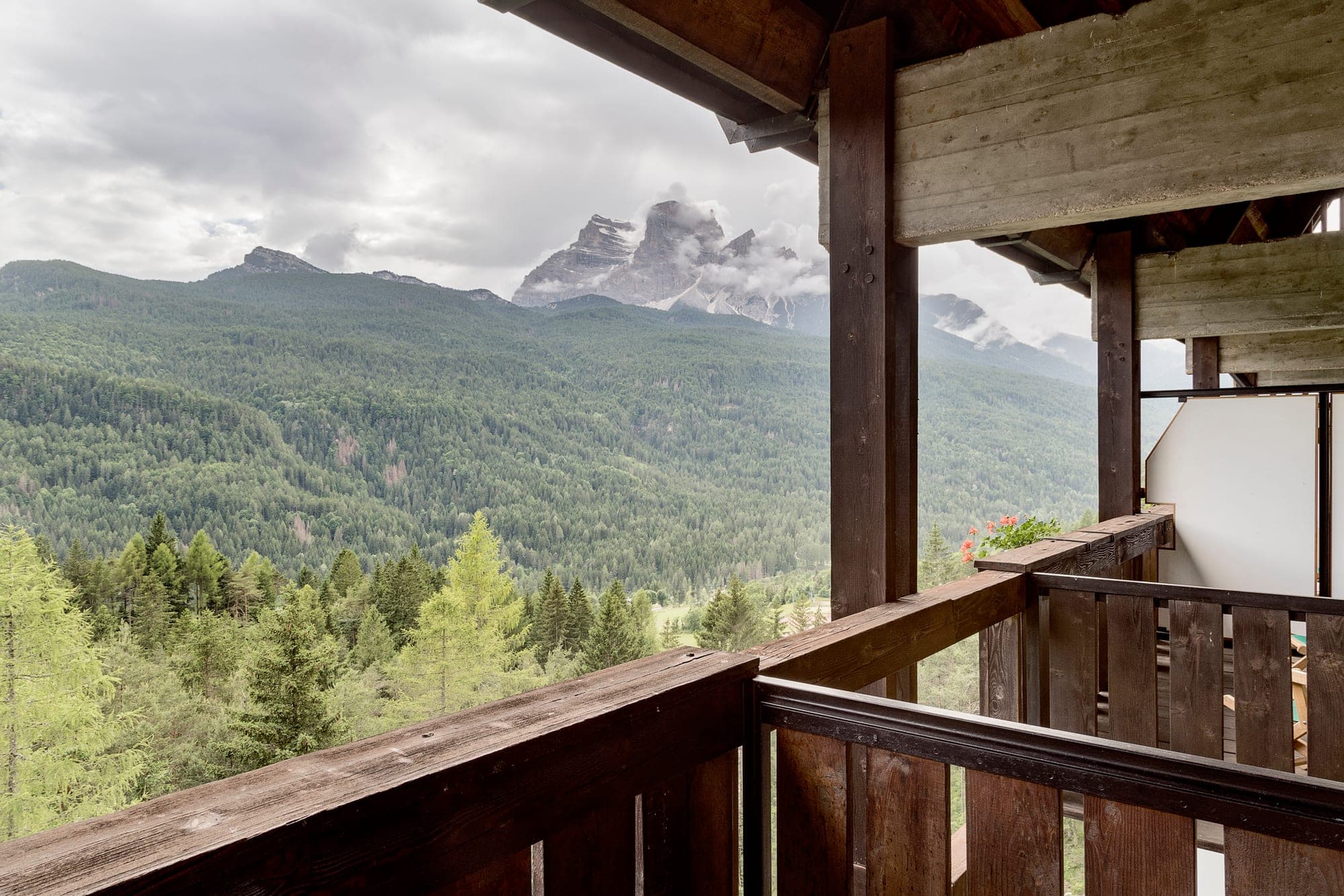 View of misty mountains and green forest from a wooden balcony.