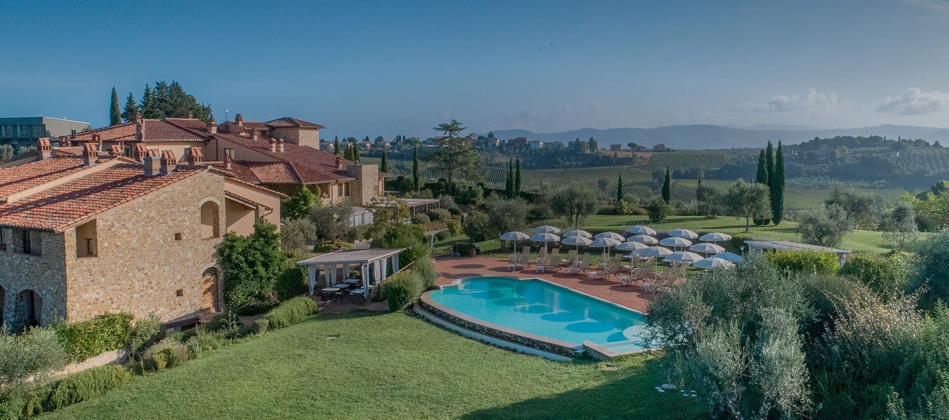 A panoramic view of Hotel Borgo di Cortefreda with a swimming pool and Tuscan hills in the background.