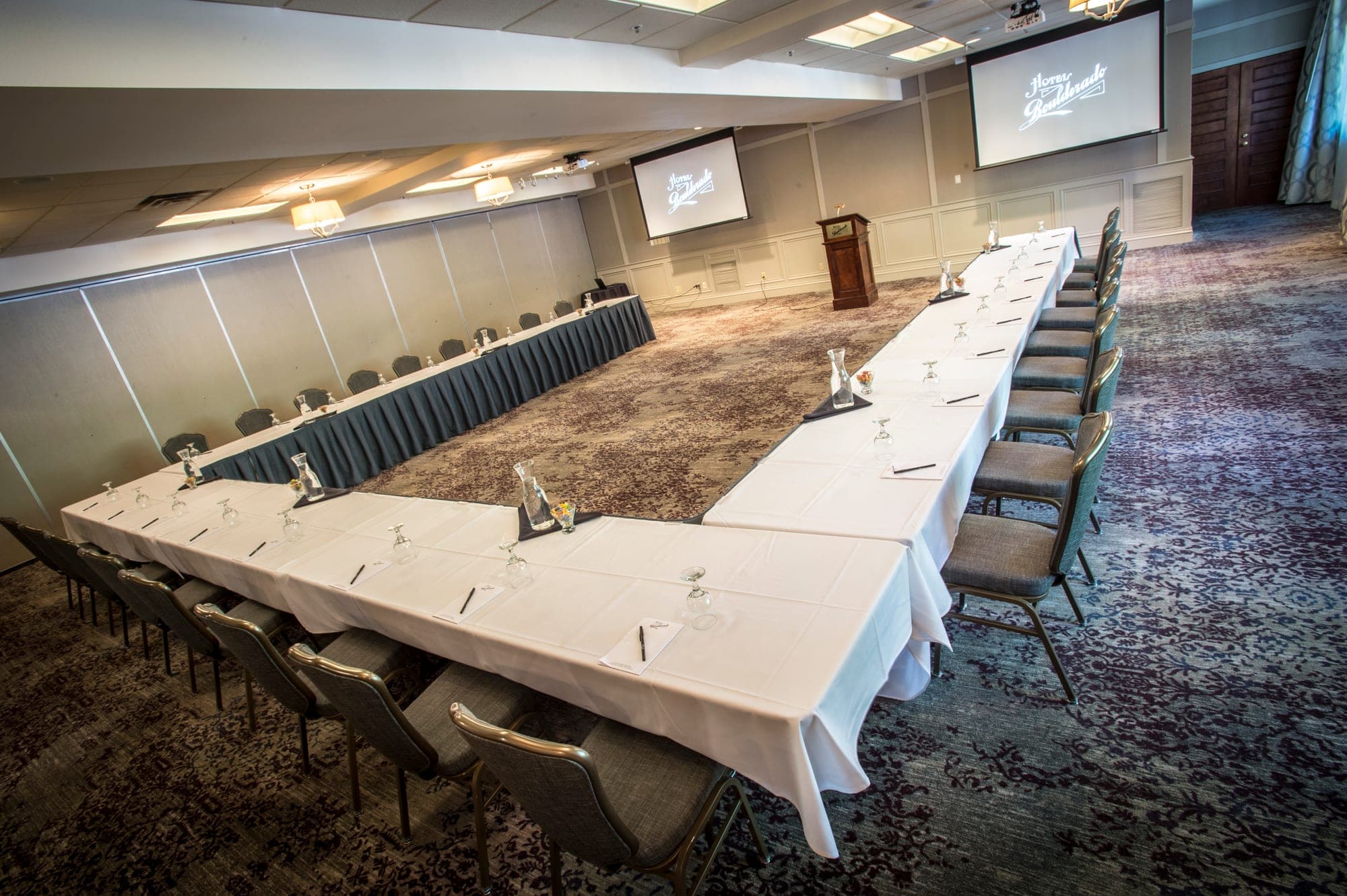 U-shaped table set for a meeting in a conference room with projectors.