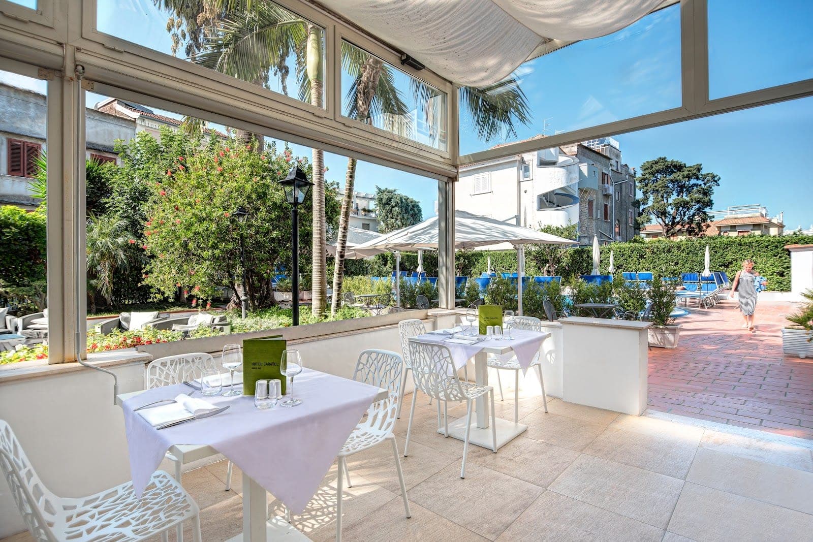 Tables set for dining on a terrace with a pool area in the background.