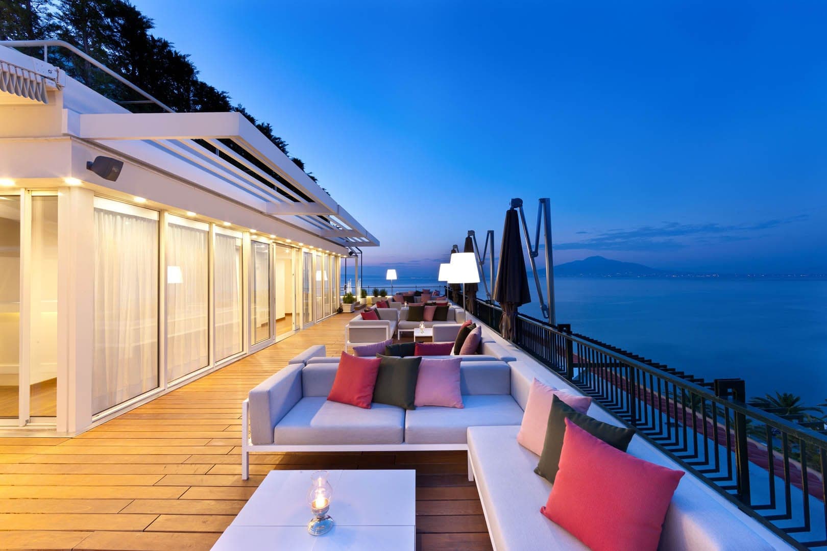 A terrace with sofas and tables overlooking the sea at dusk.