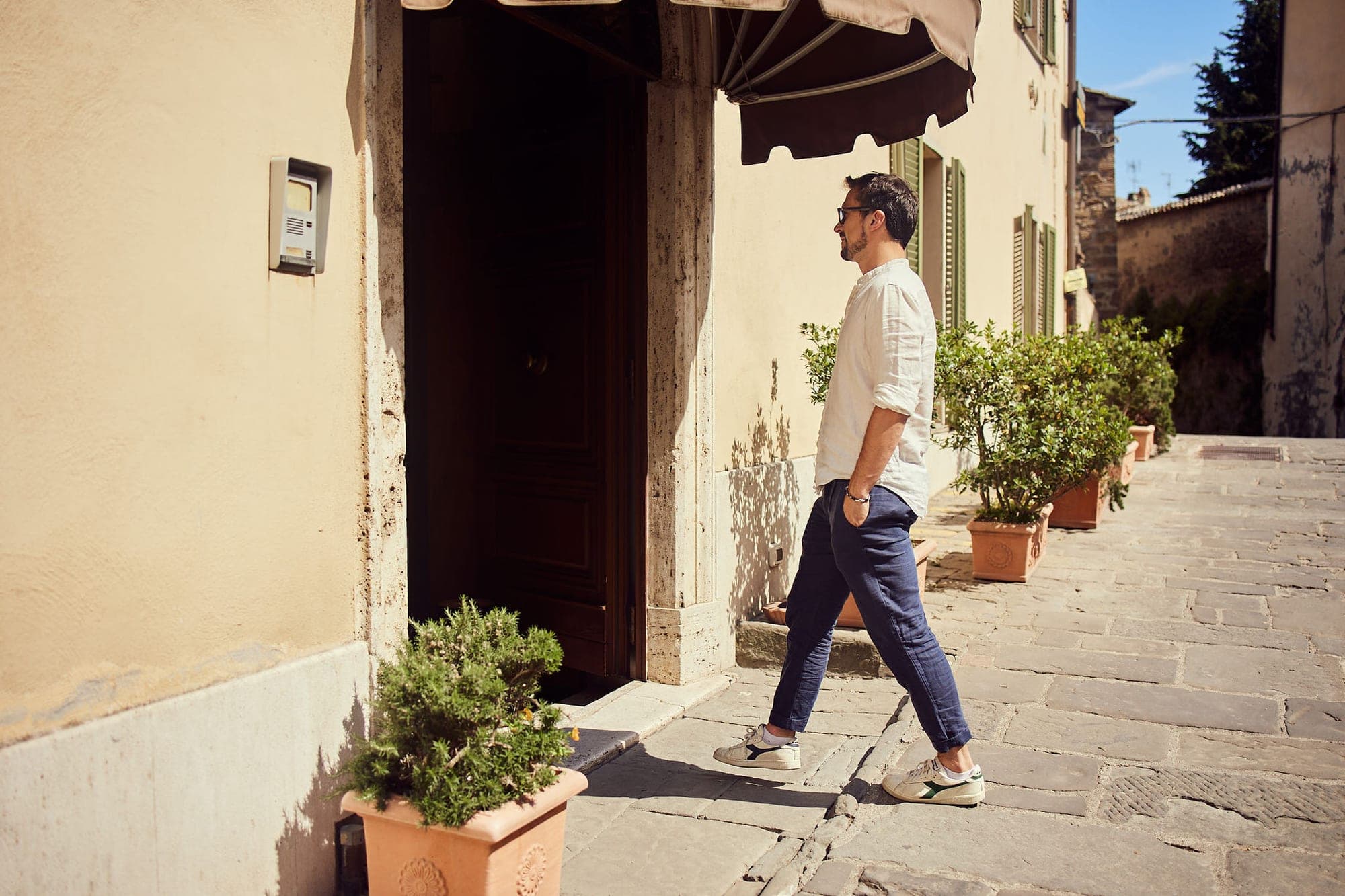 A man walks down a sunny cobblestone street in front of a building.