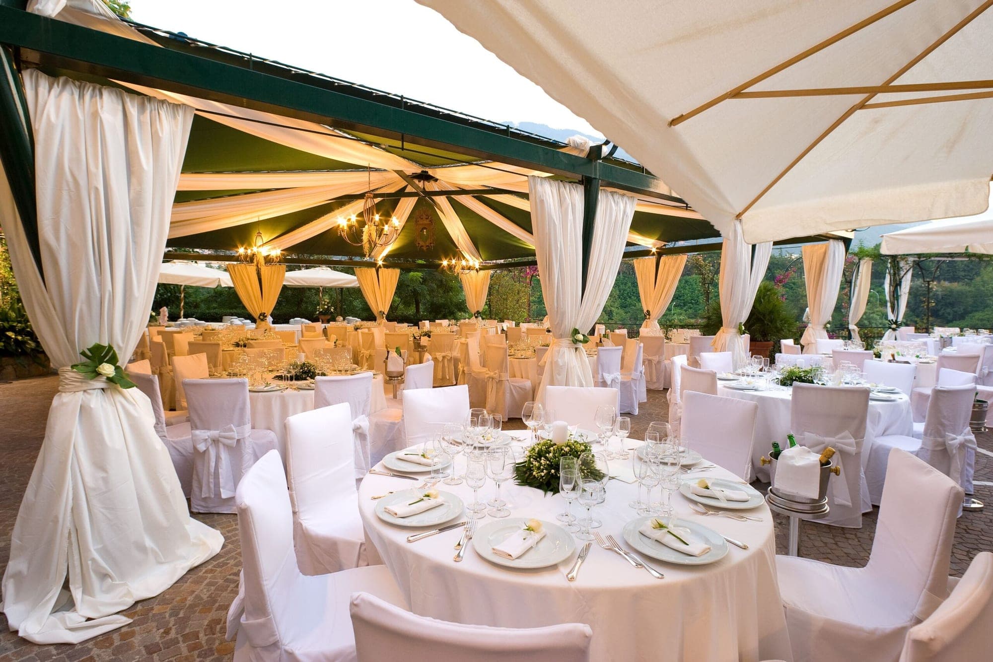 Outdoor reception area with tables set for a wedding under a draped canopy.