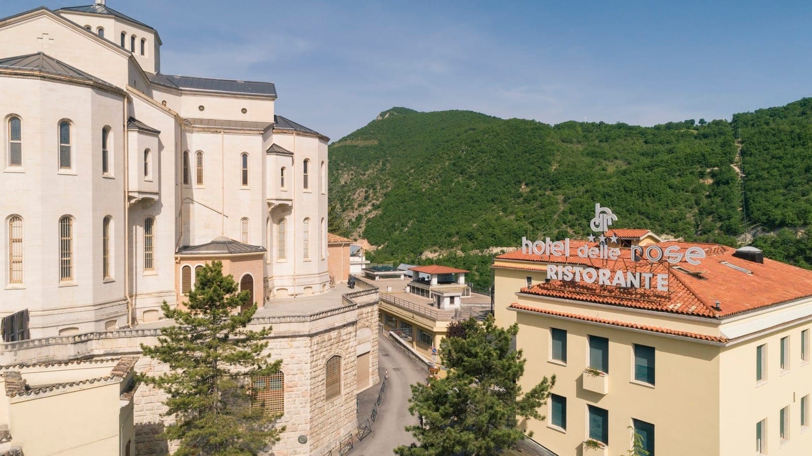 Exterior of Hotel Delle Rose with a sign and surrounding green hills.