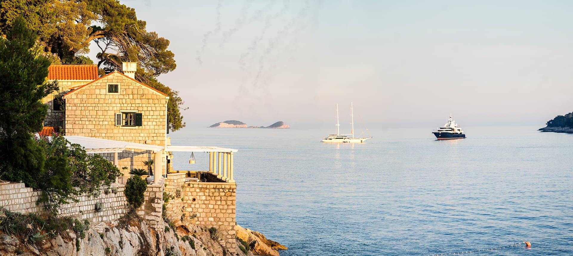 A stone building on a cliff overlooking the sea with yachts in the distance.
