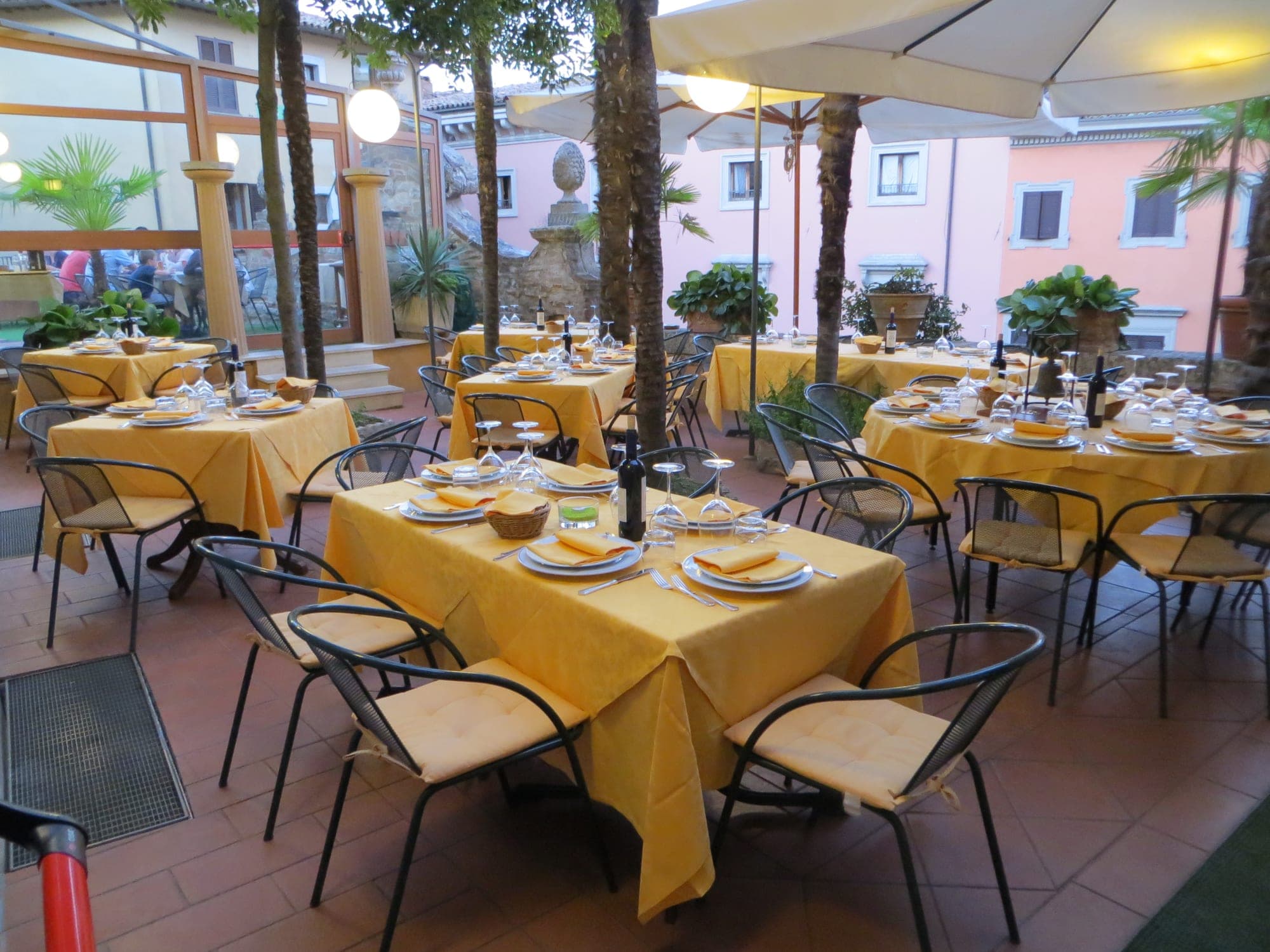 Tables set for dining in an outdoor courtyard with yellow tablecloths.