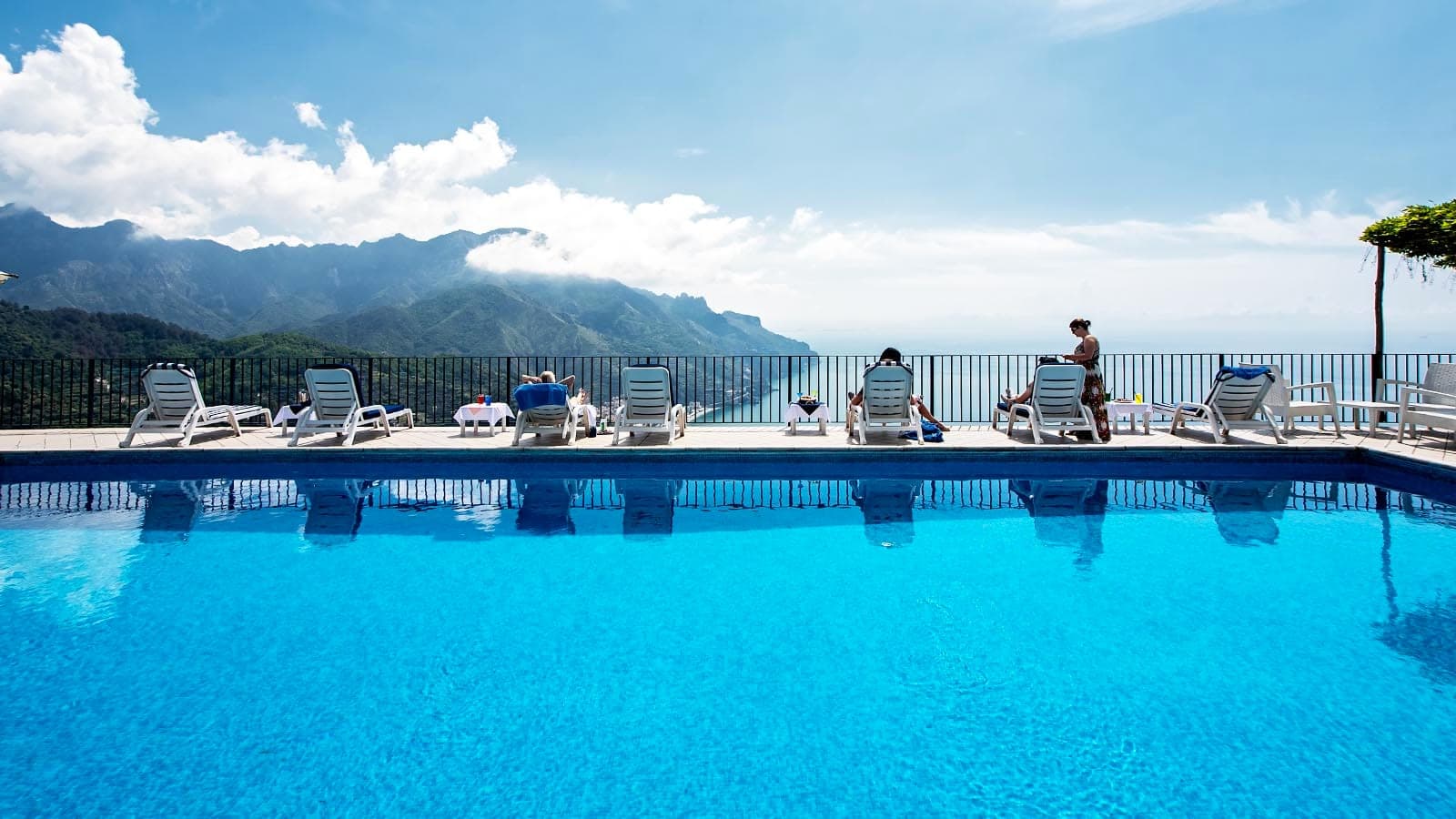 Swimming pool with lounge chairs and a view of the sea and mountains.