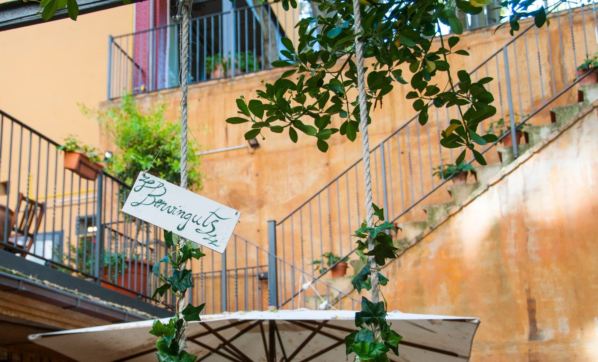 A swing with a welcome sign hangs in a courtyard with stairs and balconies.