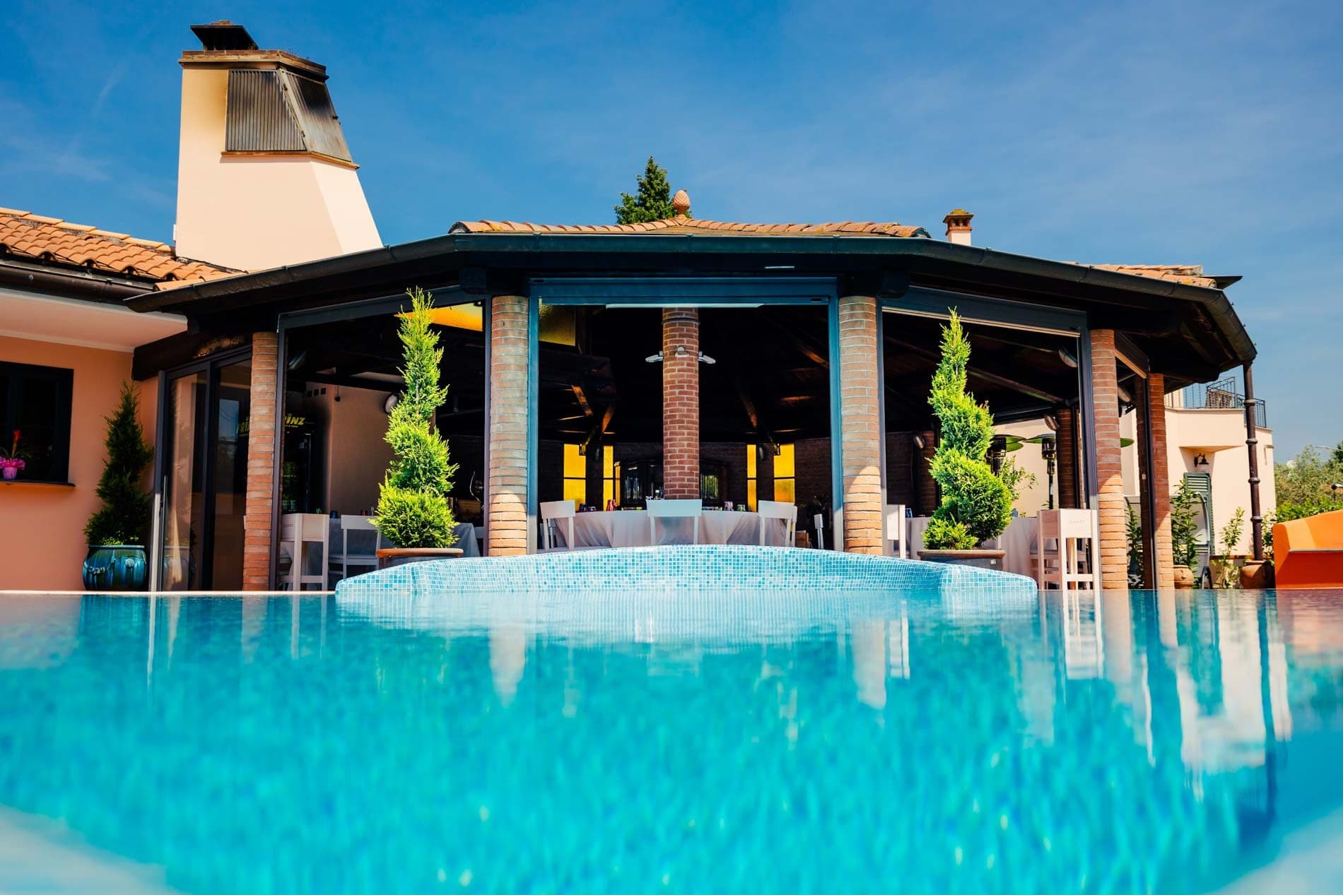 A swimming pool in front of a building with an outdoor dining area.