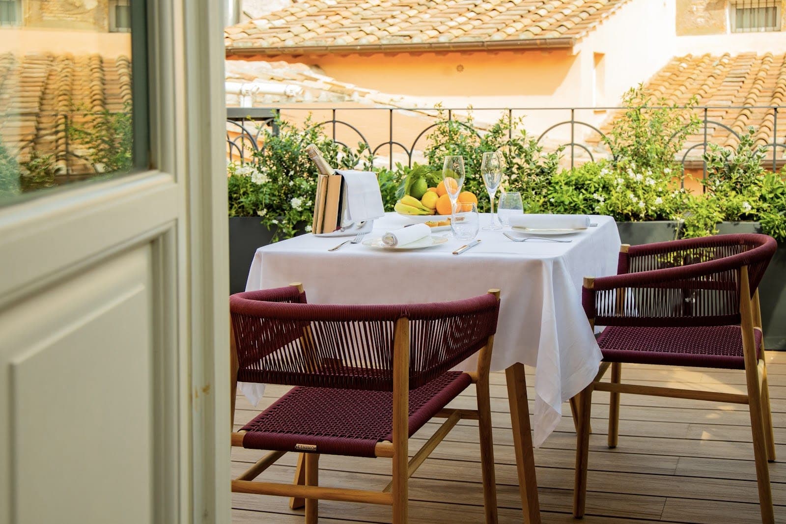 A table set for dining on a terrace with chairs and greenery.