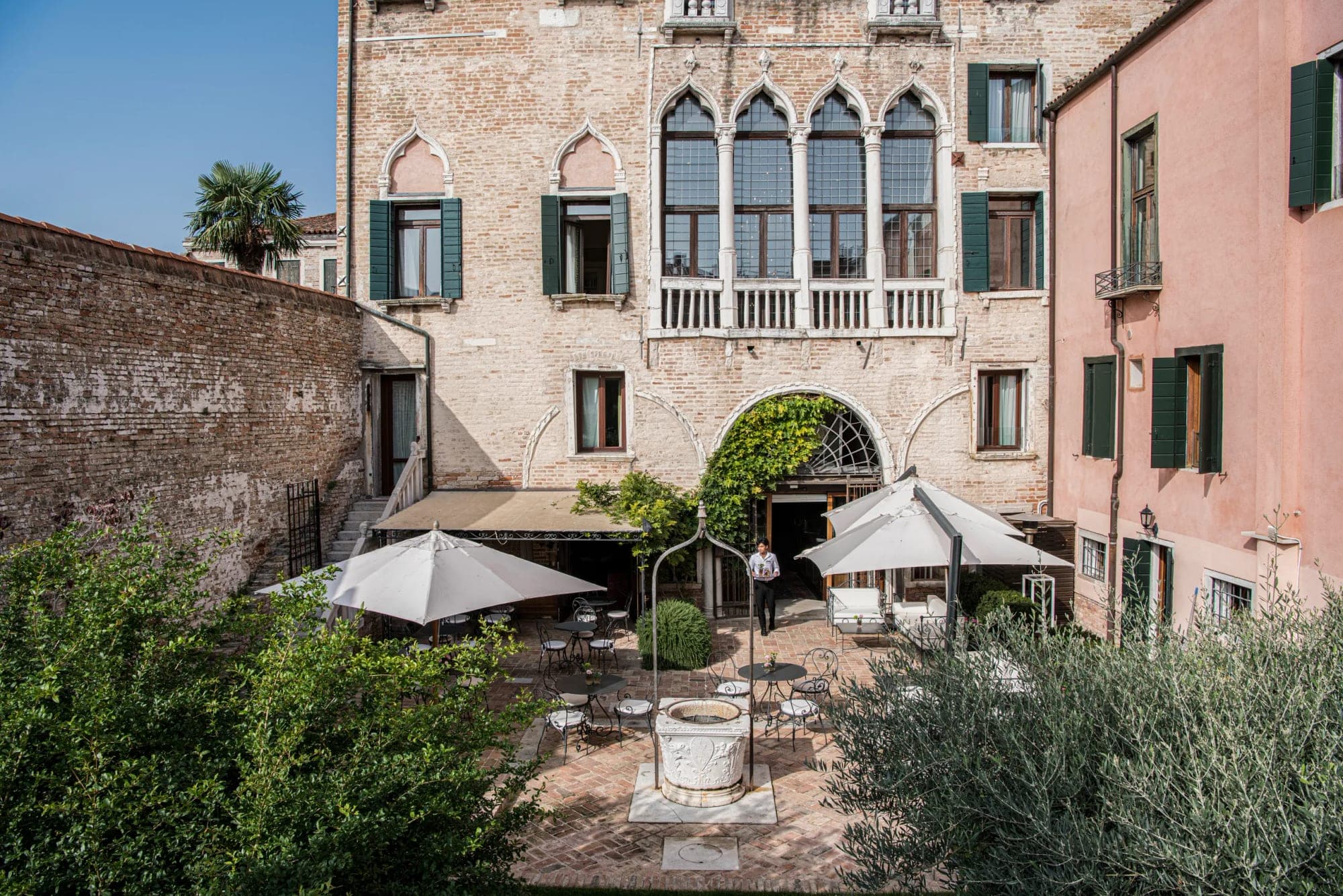 Courtyard of a Venetian building with a well and outdoor seating.