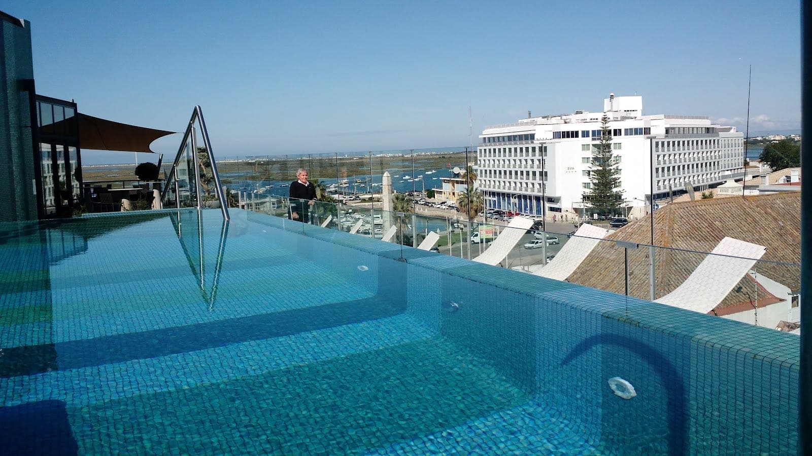 A rooftop swimming pool overlooks a bay with boats and buildings.