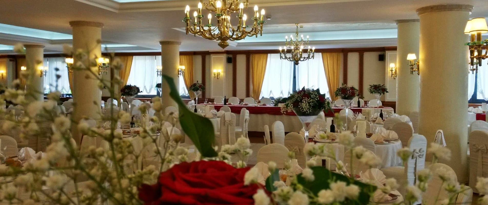 A wedding reception room with tables set for guests and chandeliers overhead.
