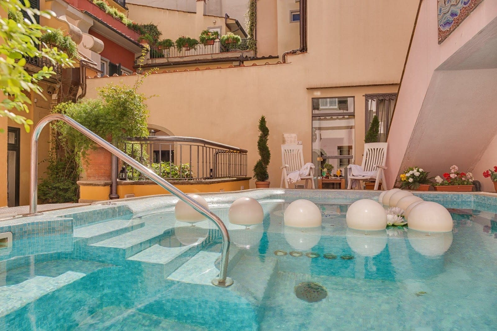Jacuzzi with steps and floating spheres, surrounded by lounge chairs and greenery.