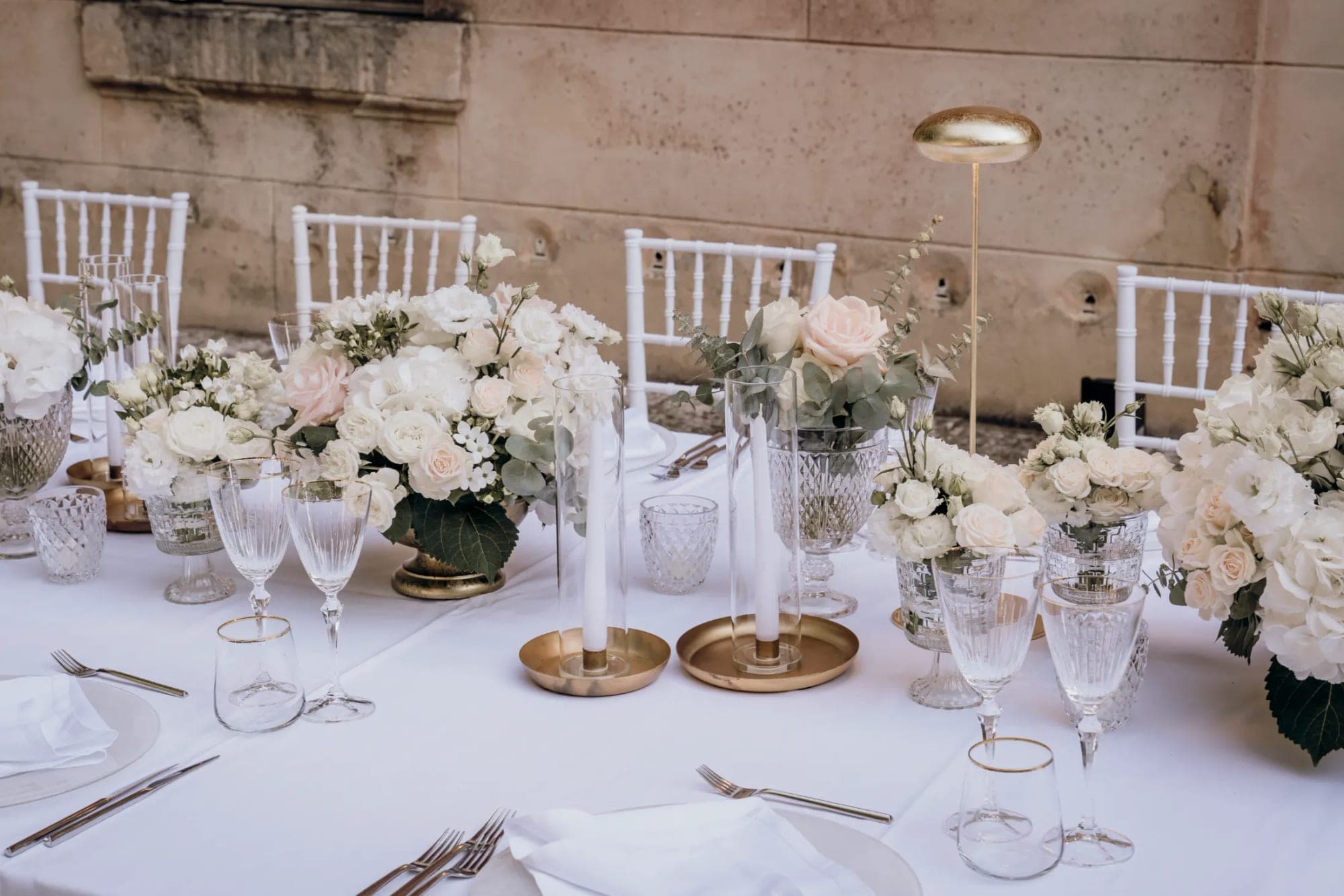 A wedding reception table set with white linens, floral centerpieces, and place settings.