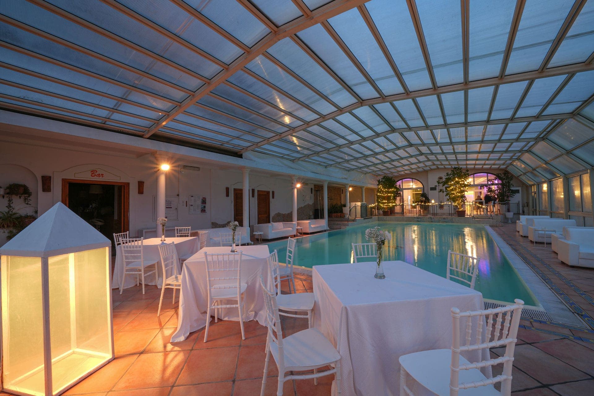 Covered swimming pool area with tables and chairs set for a reception.