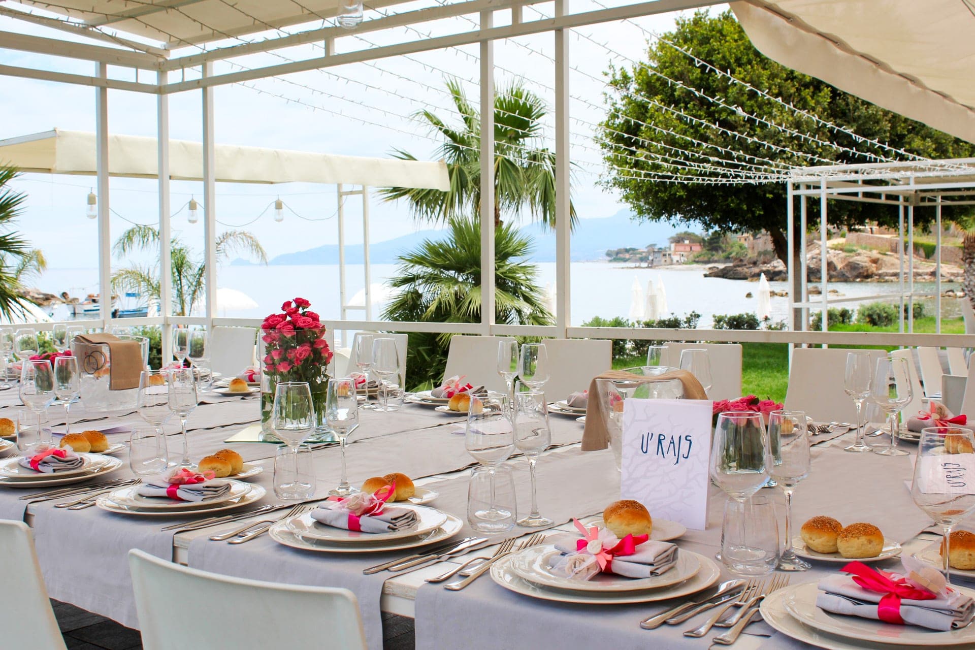 A wedding reception table is set for guests with a sea view in the background.