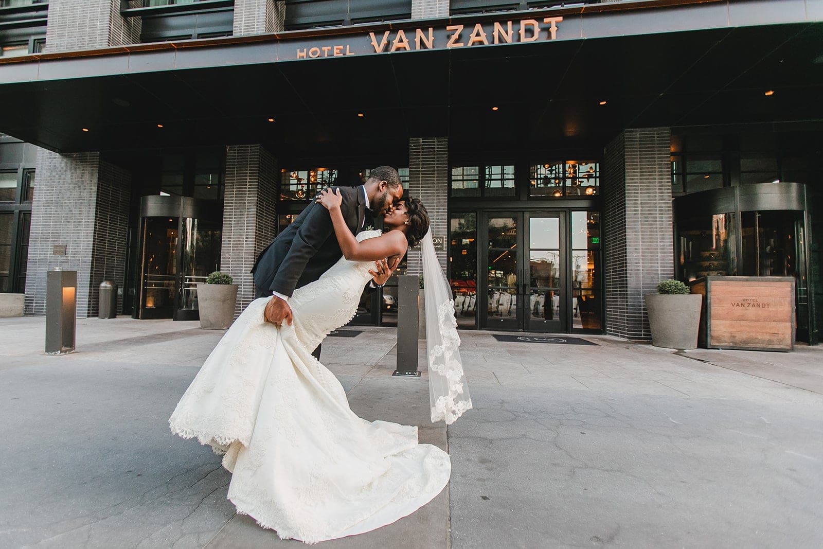 A bride and groom kiss in front of the Hotel Van Zandt entrance.