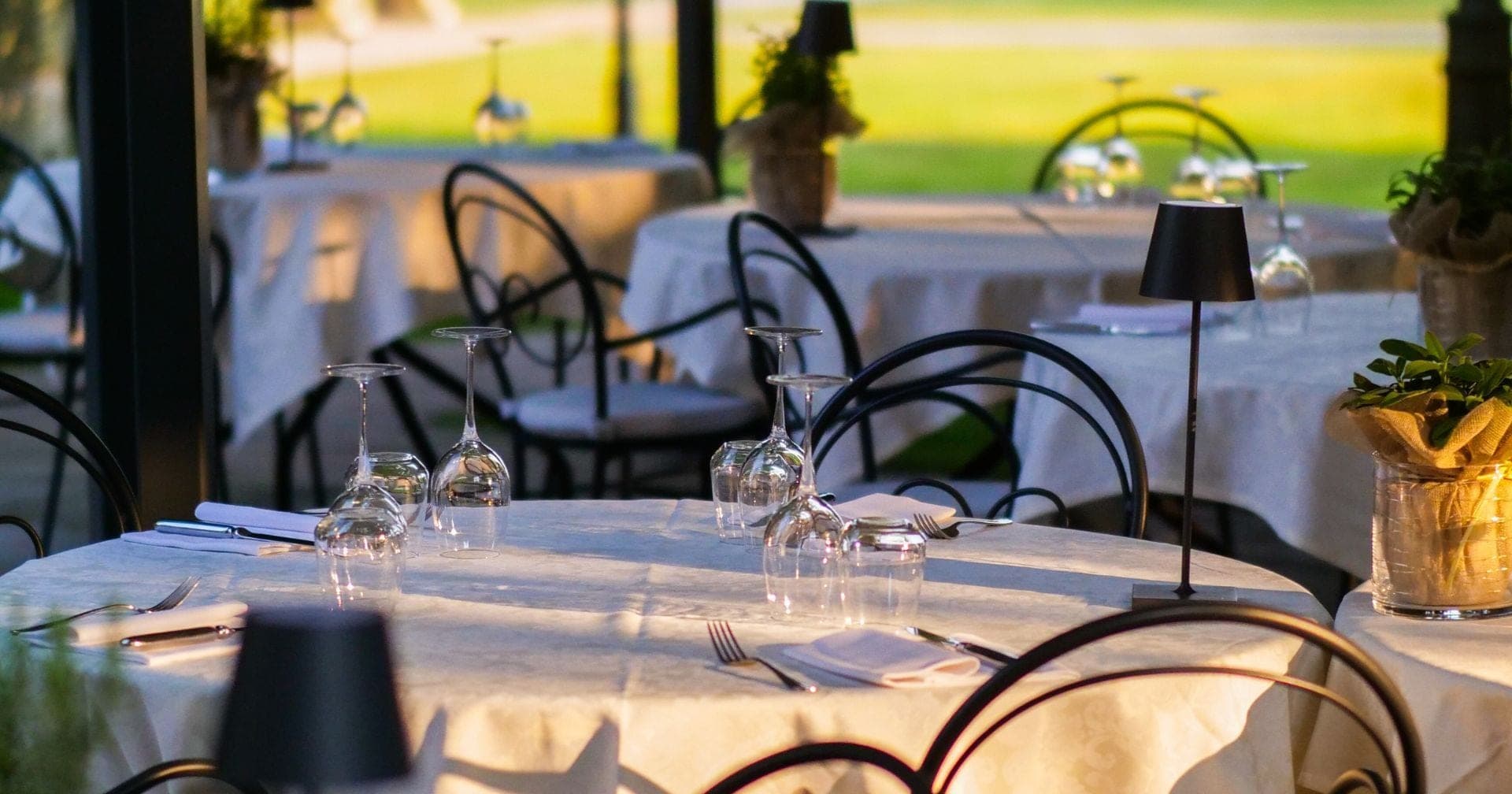 Tables set for a reception outdoors with white tablecloths and glassware.