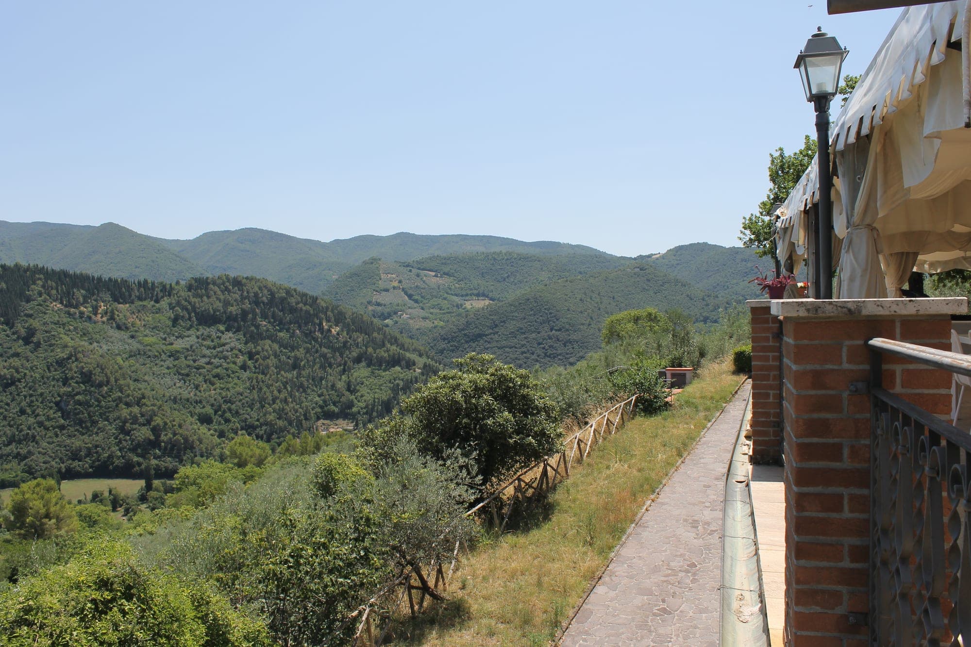 View of green hills and trees from a terrace with a lamppost.