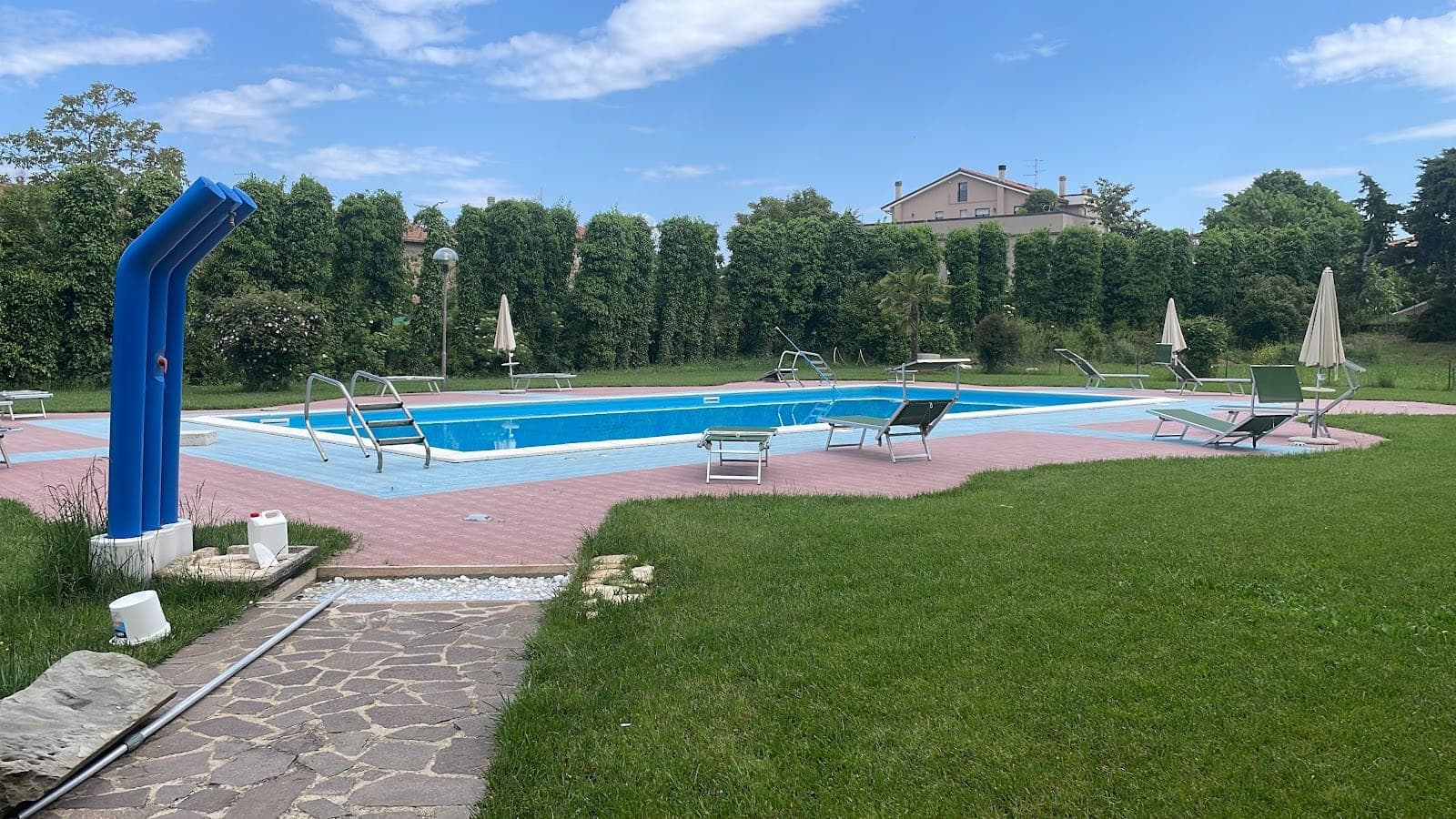 A swimming pool with blue water, surrounded by a pink and blue tiled deck and green grass.