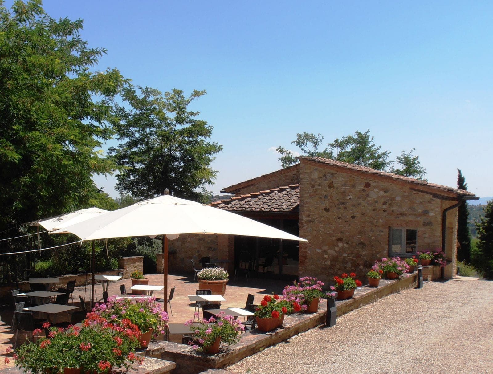 Outdoor terrace with tables, umbrellas, and flower pots at a stone building.