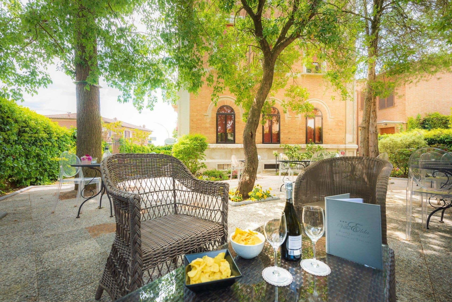 A table with drinks and snacks on a patio with chairs and a building in the background.