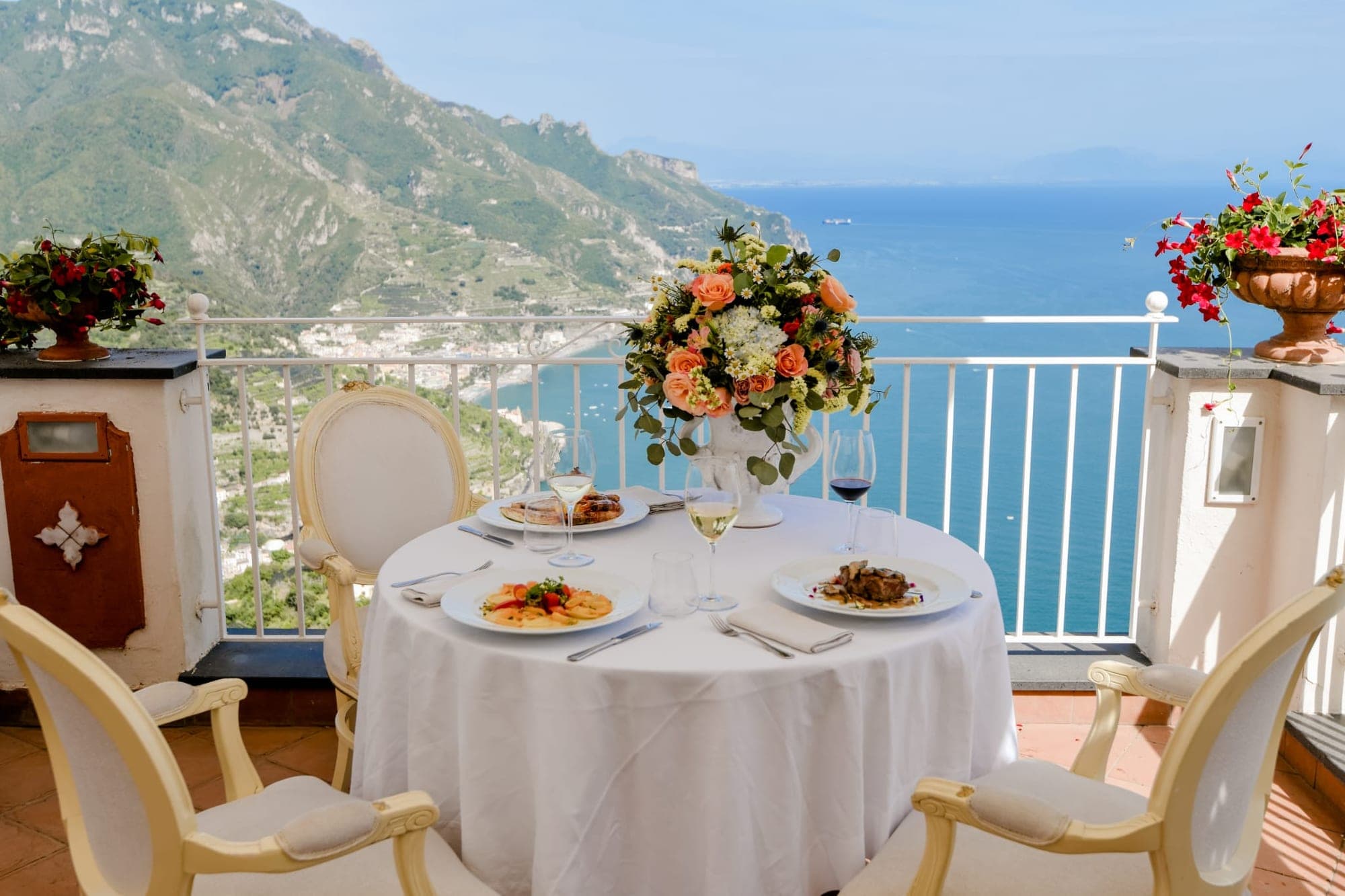 A table set for a meal on a balcony overlooking the sea.