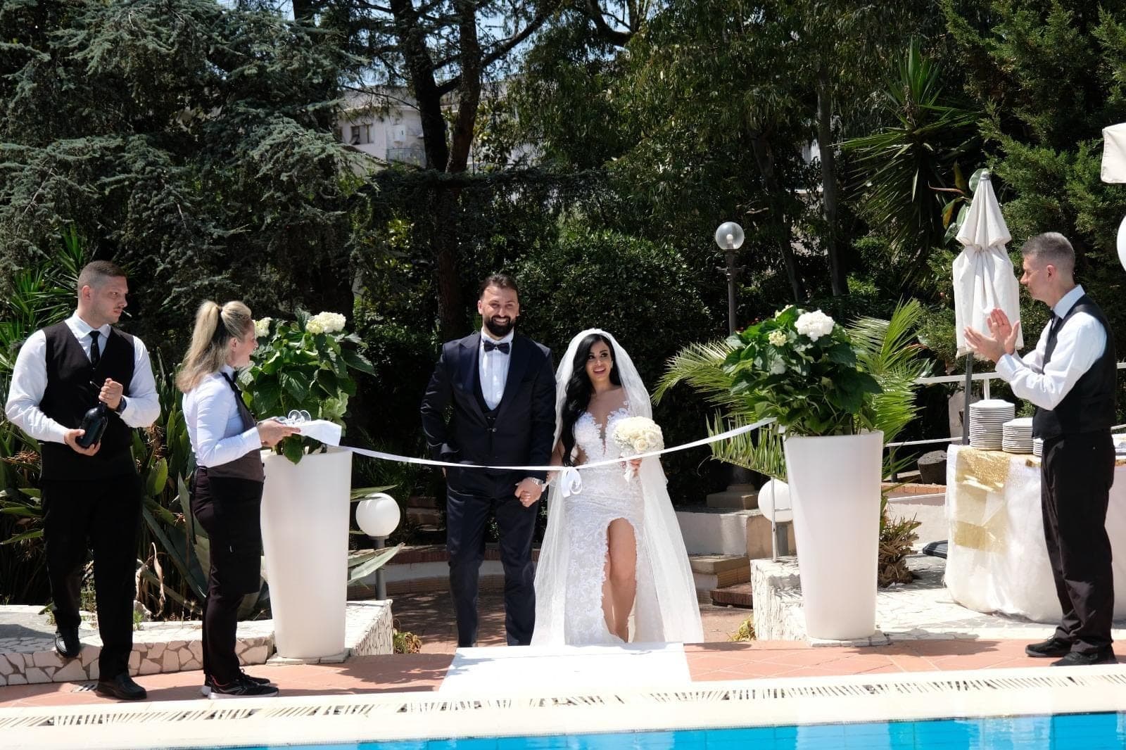 Wedding couple walking down an aisle next to a pool with staff.