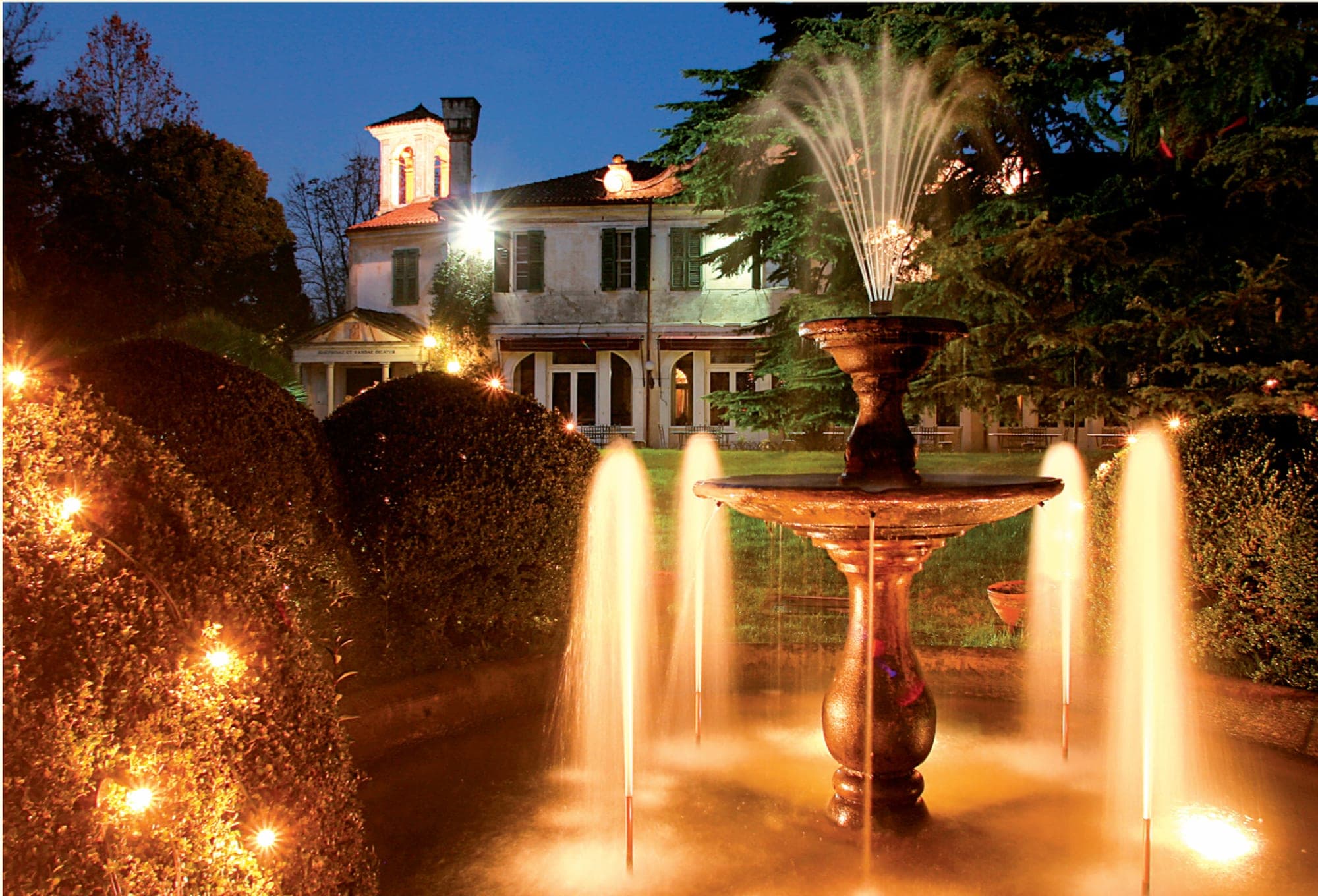 A fountain sprays water in front of a building at dusk.